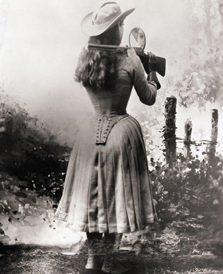 Sharpshooter Annie Oakley shooting over her shoulder using a hand mirror. Photographed in 1899.