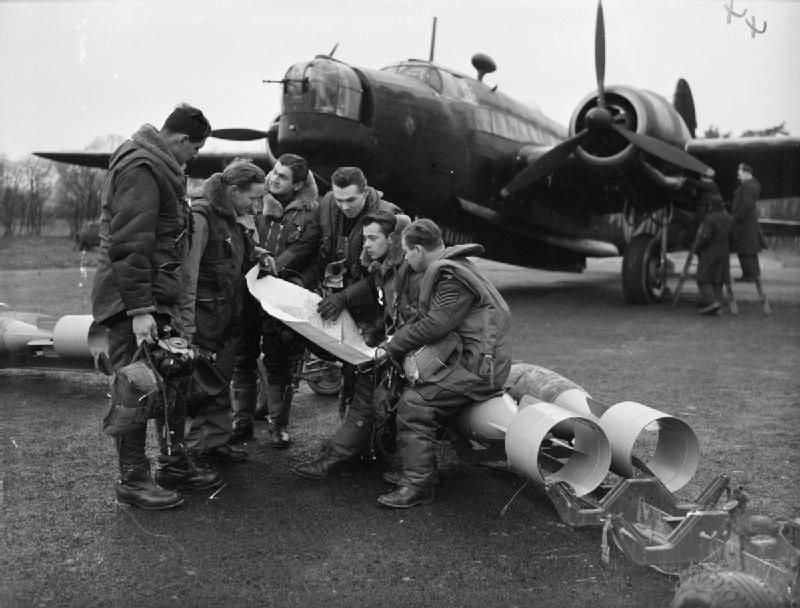 Retromania_Jr's tweet image. A #bomber crew of No. 311 (#Czechoslovak) Squadron RAF study a map, while sitting on 250-lb GP bombs which are about to be loaded into their Vickers Wellington Mark IC at RAF East Wretham, #England, in 1942.