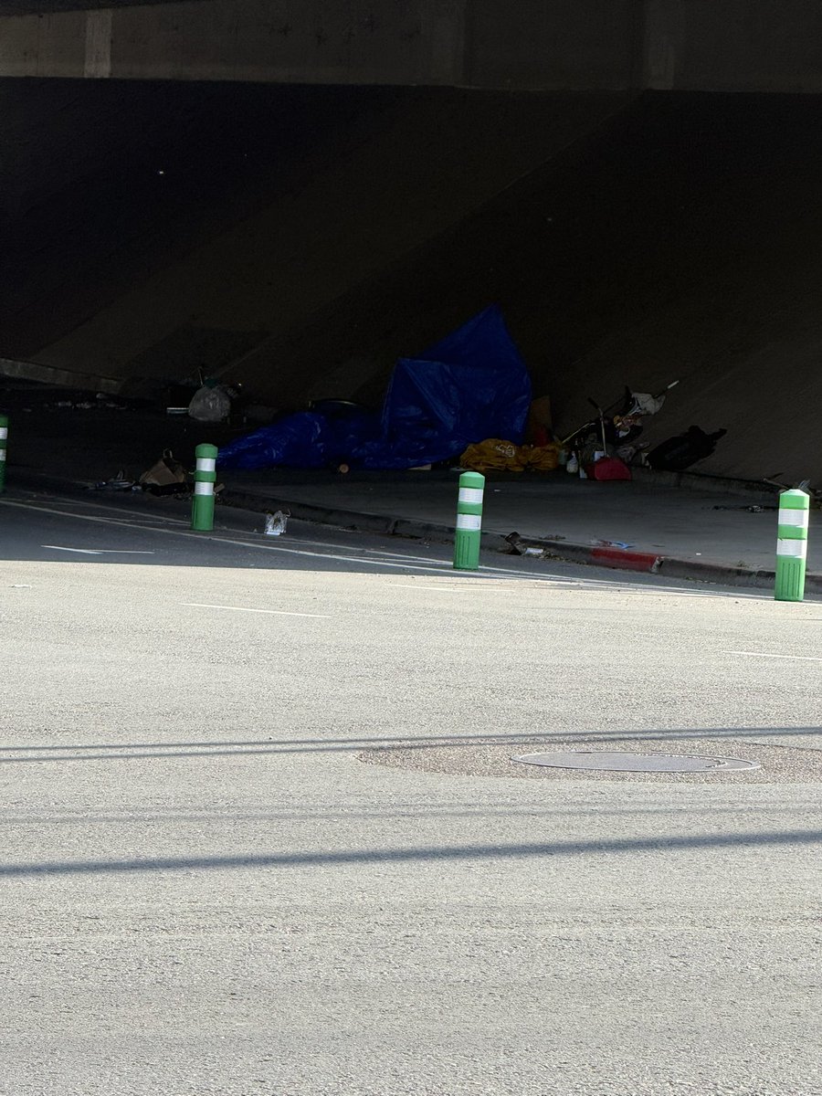 SacWalkSafe's tweet photo. Gotta lead on a 💩🎪 on 10th st underpass after posted my farmers market. Was sent this picture. I’ll check it out for 33/100 #ThisIsNotNormal mañana. @Adventuring_RE @LukeSlywaker check out trash falling into dedicated bike lane. #ActiveTransport. Adding pic from farmers market from Slow Streets tablers about potholes. Fill em with Mamdani’s face I guess