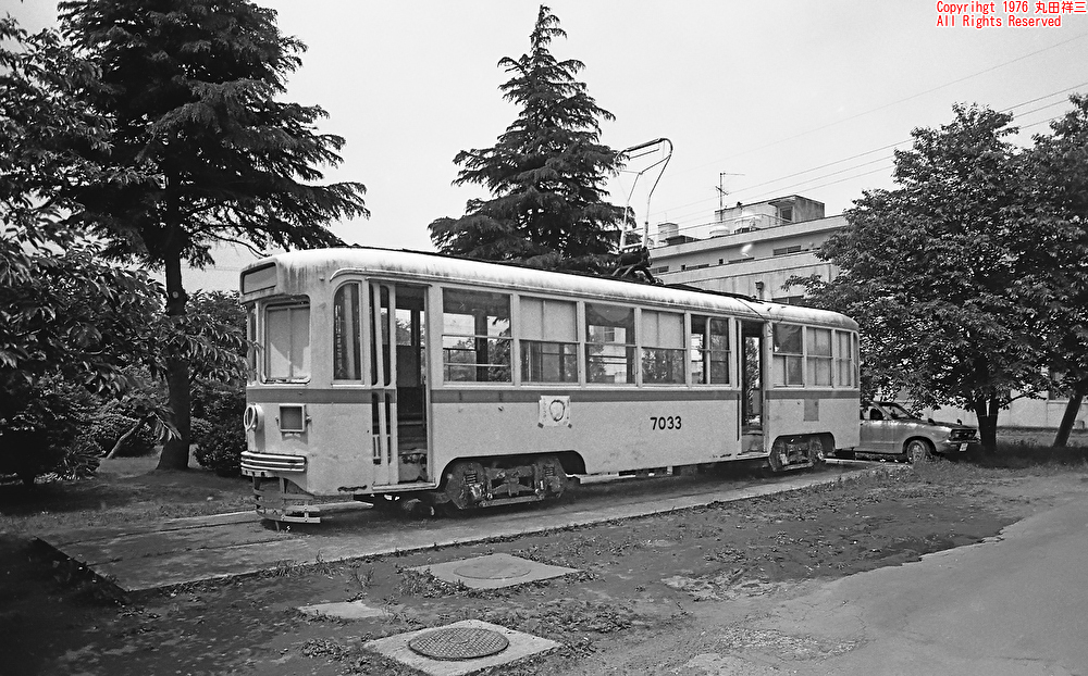 malta_shozo's tweet photo. 【新刊“廃線だけ” 未掲載作品】東京都電7000形7023号の謎 昭和51年 千葉
初公開の写真です。撮影は今から50年前の1976年夏。場所は東京都養育院千葉分院（1979年、東京都養育院千葉福祉ホームに改称、1997年に東京都福祉局千葉福祉園に改称）の中庭。東京都養育院は明治期の設立、ハンディを負った方々を保護する施設でした。
この7000形電車、展示された当初は“7030号“となっていたそうで、後に“7033号“に書き換えられたらしいのですが、本当は「7023号」です。（本物の7030は67年に目黒車庫で除籍となり、直後に解体。7033は70年に荒川車庫で除籍、函館市電に譲渡され、この頃まだ活躍中でした）
東京都電7000形7023号は1954年製。老朽化した1000形の下回りを流用し、製造されました。神明町車庫を塒に活躍を続けましたが、1968年に引退。その後、美濃部亮吉東京都知事の計らいで、養育院の子どもたちに寄贈されました。台車はベースとなった1000形電車のD-10形を流用しています。
何故再三ナンバーが書き変えられたかは謎ですが、当時のミステリー小説では、“戦中戦後の混乱期に他人になりすます“といった展開が多かったので、色々ドラマチックなストーリーを空想したものです（笑）後ろに駐車している日産サニーB210も懐かしいですね。電車は後に姿を消しました。

この写真は私の書籍『廃線だけ―平成・令和の棄景』の続巻『廃線だけ―昭和の棄景』用にデータ化した一枚です。（書籍には掲載しておりません）

■昨夏発売『廃線だけ―平成・令和の棄景』
https://t.co/iw4a78neuK
平成・令和に残る廃線を美しい写真で紹介した決定版。上のurlは実業之日本社による紹介ページです。こちらからオンライン書店にも飛べます。Amazonでも再び入手可能となりました。重版分の印刷も最高レベルの仕上がりです。現在、三刷り（二度目の重版）も出来しております。この機会にぜひ、お手に取って頂けましたら幸いです。

■昨秋発売の続刊『廃線だけ―昭和の棄景』
https://t.co/qiinoqHXtw
昭和の懐かしい廃線風景をまとめた『廃線だけ―昭和の棄景』は昨秋発売されました。印刷に立ち会いましたが、素晴らしいクオリティでした。製本も凝った仕上げで、最高の一冊です。紹介ページからAmazonにも飛べますので、ご注文頂けましたら幸甚です。

街歩き好き、写真好き、廃墟・廃線好き、鉄道好きの皆さま、ご高覧頂けましたら嬉しく存じます。

#都電 #東京都交通局 （※荒川線に残った7000形は、1977年の車体更新の折、車体番号を新たに付番されています。本文はそれ以前のお話とお考えください）