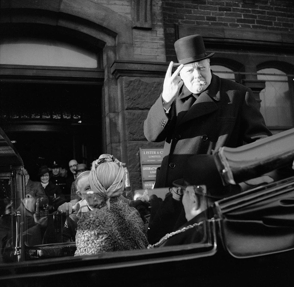 Winston Churchill gives a V for victory sign, unaware of the offensive meaning of holding up his hand in that gesture, only learning in 1943 when a secretary informed him of its meaning. It took him some time to adjust, still doing it sometimes in 1943. | Bradford, England. Dec…