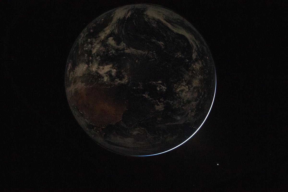 The Earth is seen mostly in shadow, with lights visible down below and just a hint of light reflecting off one edge.