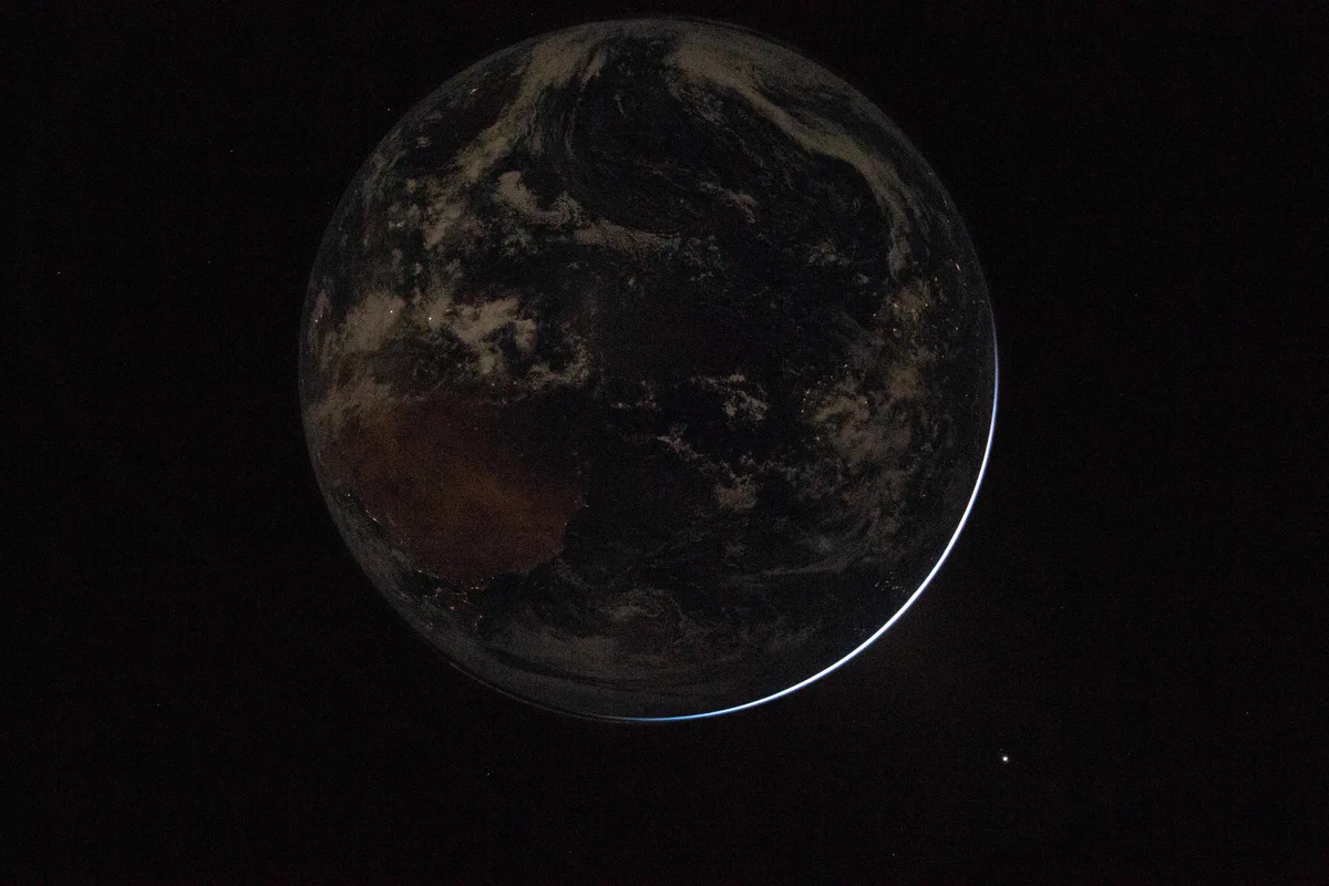 The Earth is seen mostly in shadow, with lights visible down below and just a hint of light reflecting off one edge.