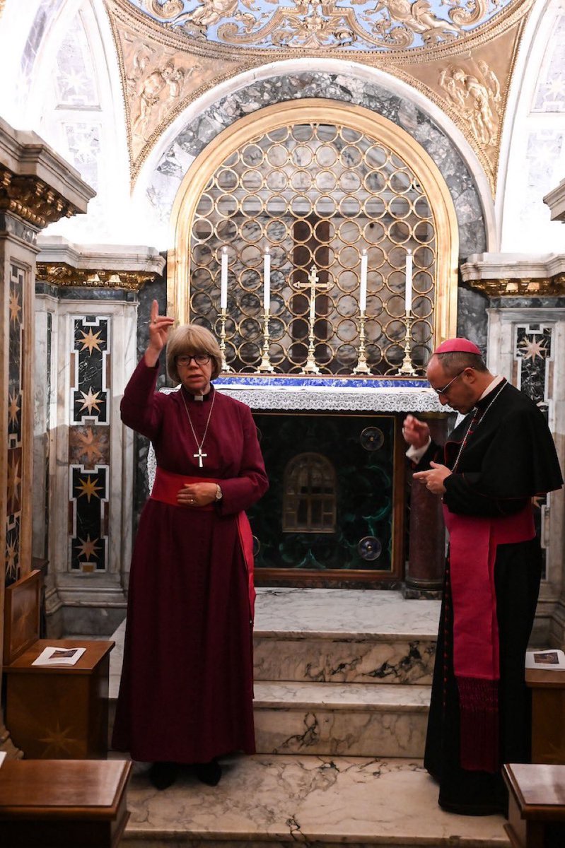 La “Arzobispa” de Canterbury finge impartir una bendición en la Capilla Clementina, en la cripta de la Basílica de San Pedro del Vaticano. Es la capilla más cercana a la tumba de San Pedro.

A su izquierda, un obispo católico fingiendo recibir la “bendición”.

El lunes por la