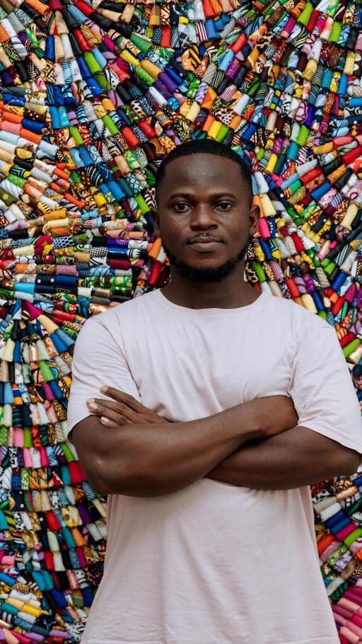 ghanaspora's tweet photo. 🇬🇭Emmanuel Aggrey Tieku is a 31 year old artist who works between Accra and Paris. He has spent years transforming discarded textiles into large scale installations. Baleboard is the project that takes this practice into public view by replacing commercial advertising with cascading textile waste. These works are installed on the same billboard structures that typically promote consumer products.

Tieku stated that galleries tend to confine discussions within their walls, whereas billboards allow conversations to unfold in public spaces. Ghana receives approximately 15 million second-hand garments every week. Around 40 percent are unsellable. This waste frequently ends up in drainage systems, coastal lagoons, and the sands of Jamestown Beach. Tieku told AFP that if waste is not visible, it fades from awareness. He noted that the project brings this reality back into focus