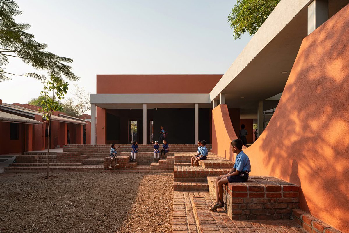 shavnyuyngah's tweet photo. A school is not a box children sit in. It is a space that teaches them before the lesson begins.

Belgaon Dhaga School. Nashik, Maharashtra, India. Architect: Pooja Khairnar, pk_iNCEPTiON. 1,050 m². Completed 2025.

The existing school was a rigid linear block, one long row of classrooms facing an open ground. The intervention refused to repeat that logic. Instead a series of smaller blocks arranged like a village, connected by courtyards, shaded corridors and brick terraces that blur the boundary between classroom and playground.
Buildings oriented to the sun path for maximum shade. Perforated openings and louvered panels for natural ventilation. Local brick throughout. No air conditioning in a school that needs none.

The circular courtyard at the centre is not a design gesture, it is an amphitheatre, a gathering space, a flag ceremony ground, a place where the community sits in the evening.

This is what it looks like when an architect asks what children need from a building rather than what a building requires of children.