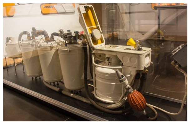 The Soviet ASU-8 toilet for Buran kept the core design but got major upgrades over ASU-VII: a proper toilet seat with integrated urinal, a large removable solid-waste container (30+ crew-days), electrical overflow alarm instead of visual checks, a more powerful fan for better