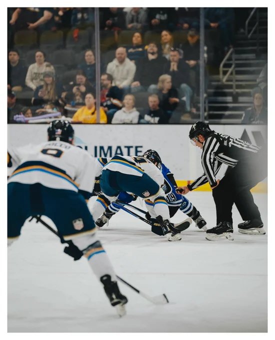 Stampede’s Cooper Soller faces off against Lincoln Stars’ Casey Vandertop as the referee drops the puck, with Thomas Zocco blurred in the foreground and fans watching from behind the glass.