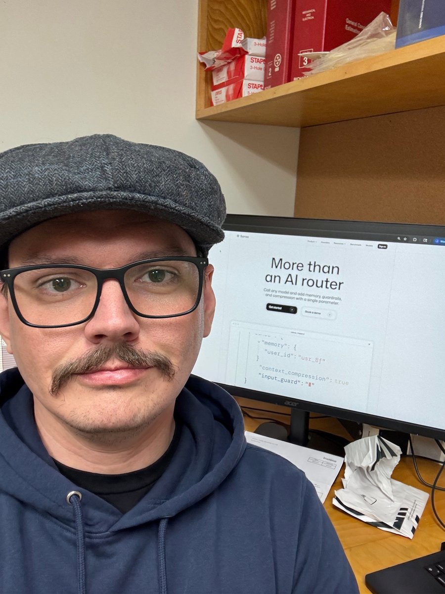 Joshua Martin, seated at a desk, the screen behind him shows a landing page with text that reads "More than an AI router"