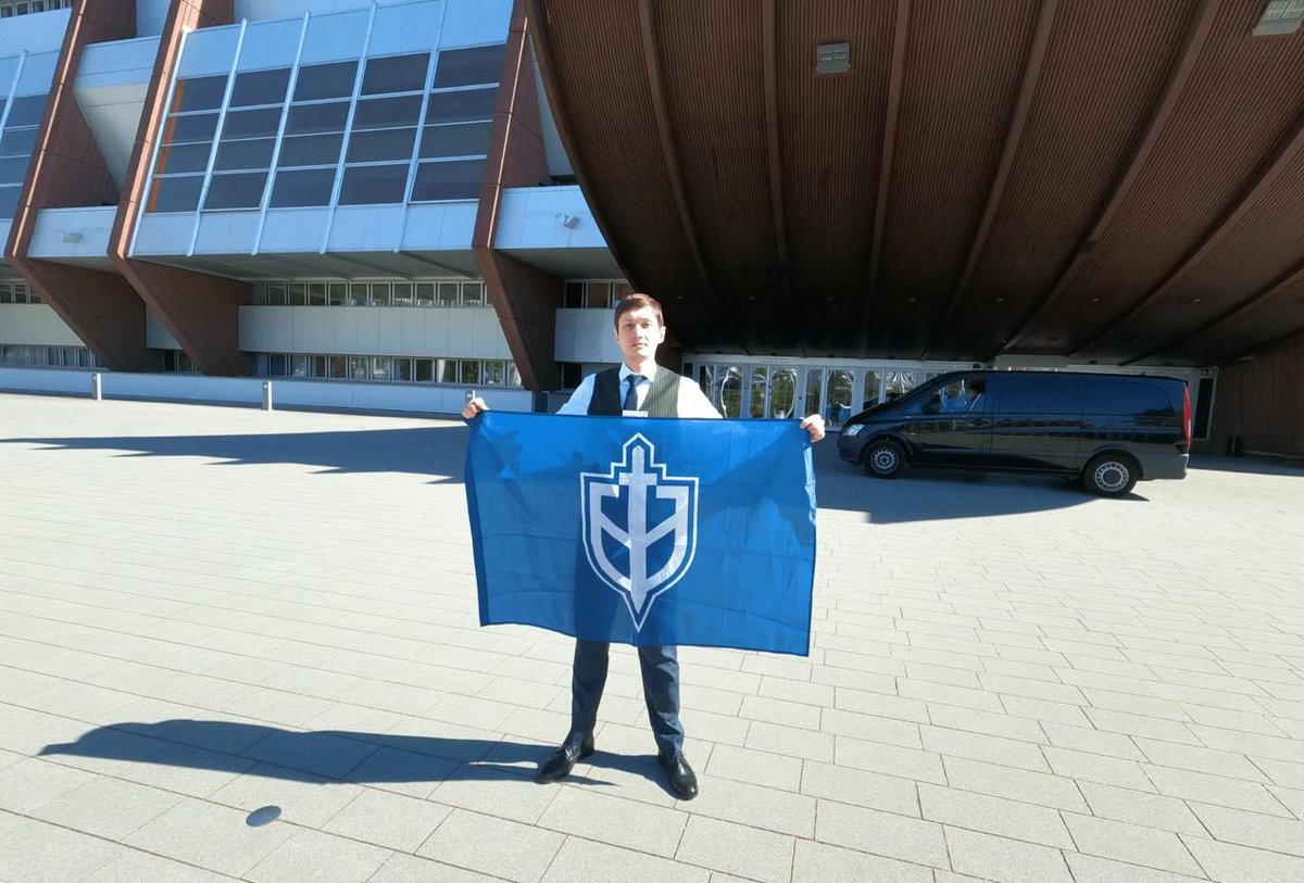 A representative of Ukraine’s neo-Nazi Russian Volunteer Corps, Pyotr Bakumov, poses inside and outside the PACE building in Strasbourg. In the second photo, he holds an RVC flag with the Spayka symbol invented by White Russian admirers of Hitler in the 1930s (in case you wonder