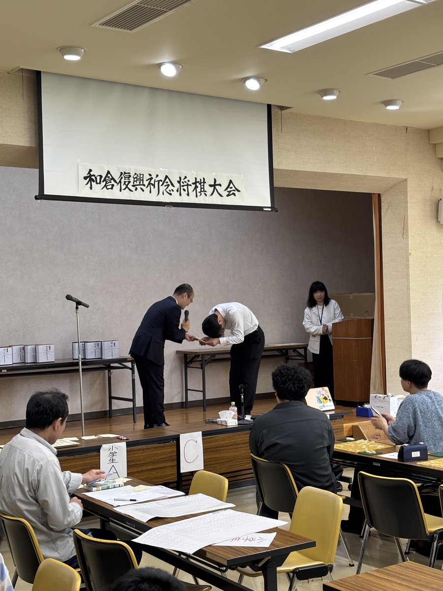 55swkk's tweet photo. #和倉復興祈念将棋大会 、参加約100人+付き添い。渡辺九段は私がいる時間帯ずっと立ちっぱなしで指導対局多面指し。指導対局を中断して行われた子供の部表彰式では、大人の部の方々が秒読みの最中でも盤を睨みながら拍手する文化がありました。ぬい贈呈式のあとに色紙チャリティのお金の贈呈式。 https://t.co/KQ6a13NIsv