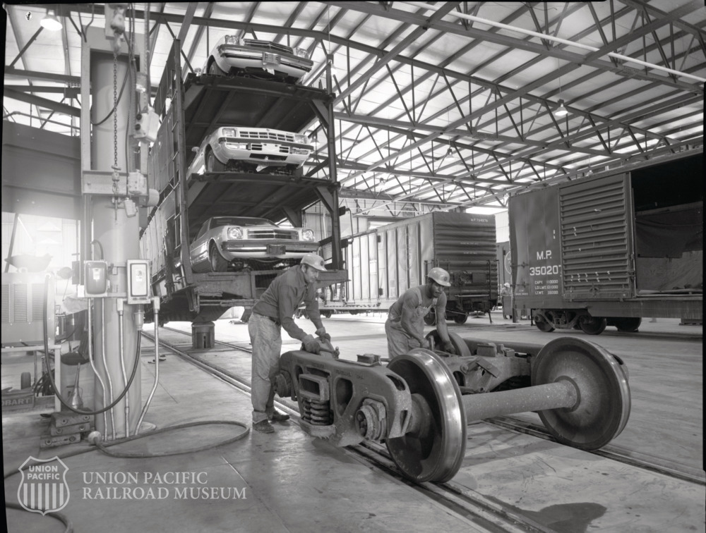 UPRRMuseum's tweet photo. Interior view of two workers in Dupo, Illinois, freight car repair shop, May 1979.  
 
Check out the automobile rack car getting lifted with the autos still loaded! https://t.co/WCzo4jsm47