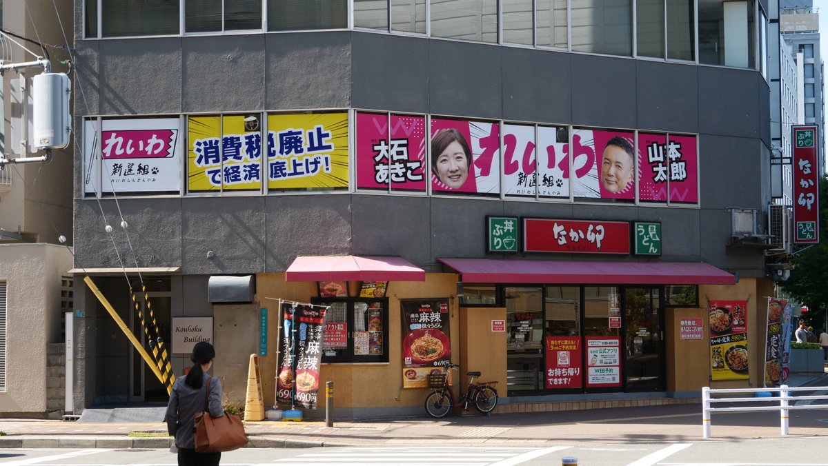 enokidas's tweet photo. 【IBB速報】西中島ダダ事務所撤退の情報がありましたが「誤報」です。やはり「看板貼り替え」でした。
#れいわ新選組 #大石あきこ #Xデー

旧タイプ（衆院議員表記あり）の看板は「ガラス窓の内側に置いてあるものが透けて見えているだけ」と強弁して公選法の制限をすり抜けたタイプでしたが、本日設置の新タイプは政治家表記が取れたことで堂々とガラス窓外面に貼り付けたものとなっています。
毒々しい色使いにより、風俗ビル感が一層鮮明になりました。
さぞや「なか卯」さんは困惑されていることでしょう。
※カジノ中止の表記も無くなりました。
#IBB #独立放送旅団 #MLS #榎塾 #fmc_radio #getsutele #市民メディア