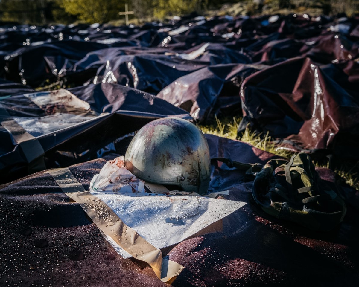 Dödrapport C.

En blodig plastficka fasttejpad med brun packtejp på en brunröd liksäck. Lappen bär namnet “Dödrapport C”. Bredvid säcken, en till säck och bredvid den ytterligare en och ytterligare en. Raderna fyller ett mindre fält. Femhundra män och kvinnor har stupat under
