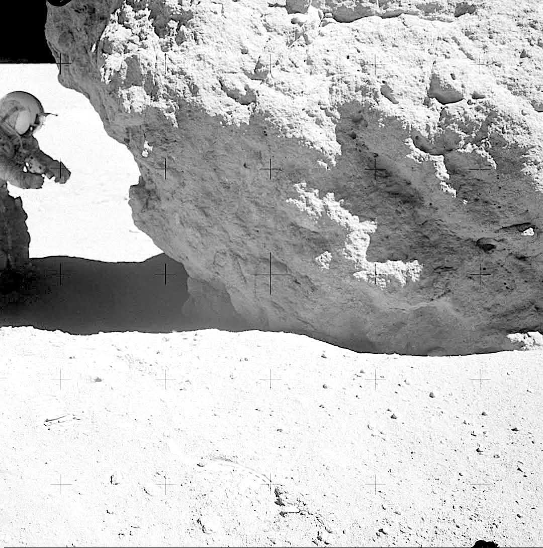 Apollo 16: John Young and the Shadowed Lunar Treasure
April 21, 1972. High on the lunar highlands at the Descartes landing site, Apollo 16 commander John Young kneels beside a massive boulder during the mission’s third moonwalk. With focused curiosity, he examines the rock at