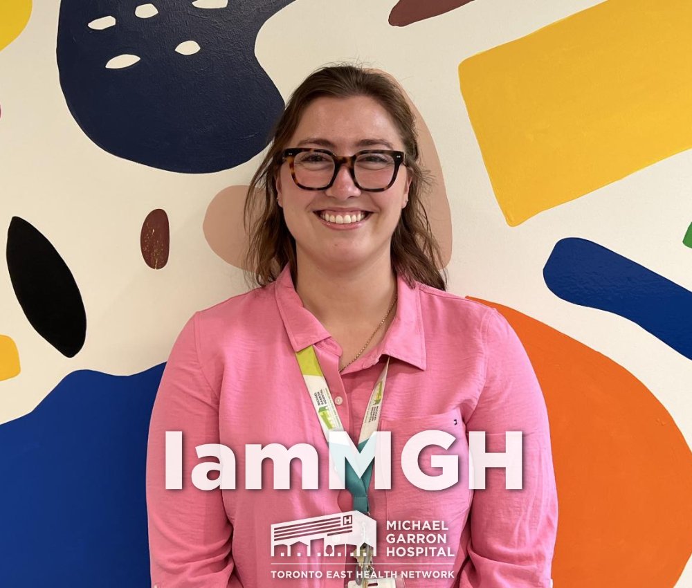 Woman stands in front of multicoloured wall with text at bottom saying “IamMGH”