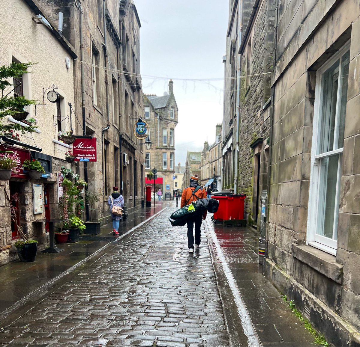 Jadler311's tweet photo. @JohnMorton215 Was going to post a picture on the Swilcan, but I love this one of a friend of mine walking through the rainy streets
of St. Andrews in search of a pint after a wild round at the Jubilee course. https://t.co/F1lss7hqKC