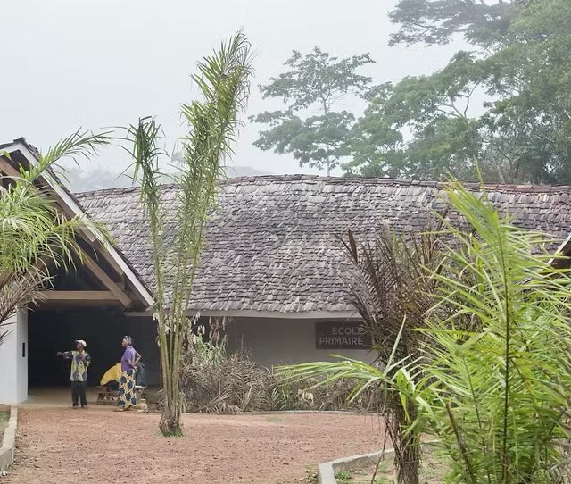 shavnyuy's tweet photo. This school is six hours by motorcycle from the nearest airstrip in the middle of the Congo rainforest. Not one building material could come in that couldn’t fit on the back of a bike.

MASS Design Group’s co-founder put it simply: “We had to build it all out of materials we could source or farm from this very site.” 

The walls are sun-dried adobe bricks made from termite mound soil, which creates stronger cohesion than regular earth. They’re plastered with a clay-sand mix, white clay rendering, and two coats of boiled palm oil; an innovation that makes the bricks water resistant.  The roof shingles were hand-cut from local trees. Doors woven from Lilian vine, dried before use to prevent shrinking.  The trusses hand-sawn and planed on site.

In exchange for the school, the community pledged to protect over 600,000 acres of surrounding rainforest from hunting, logging, and agriculture.  Architecture as a conservation agreement.

Between 160 and 170 people from Ilima and surrounding villages worked on construction. Families set up shops around the site. Two young Congolese architects were trained in sustainable building methods. 

The building didn’t only serve the community. It was built by it.

📍 Ilima Primary School, Tshuapa Province, DRC. 
Architects: MASS Design Group. 
📷 African Wildlife Foundation