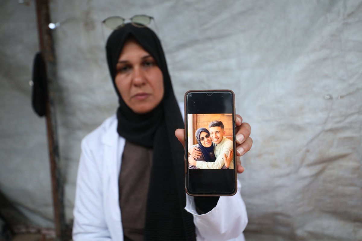 intifada's tweet photo. Surgeon Nagham Abd al-Nabi displays a photo of her and her son on a mobile phone inside a tent where she is living in Nuseirat refugee camp, central Gaza Strip, on 16 April. Abd al-Nabi’s home in the northern Gaza Strip was destroyed just before Palestinian Prisoners Day. She says her son was arrested during an Israeli raid on Kamal Adwan Hospital, where she was working and living, and is currently being held in Naqab prison. 

(📸 Hassan al-Jedi / APA images)