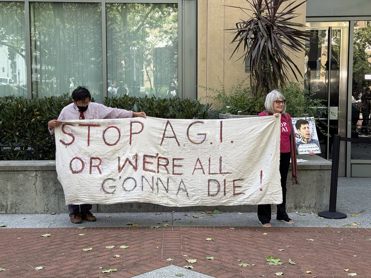 michelletomkim's tweet photo. In front of the Oakland federal courthouse, a protestor wears an Elon bobblehead, holding a bag of ketamine and a cybertruck prop, with an inflatable tube man imitating Musk in a MAGA cap. Another protestor holds a photo of Sam Altman saying “serial liar.” https://t.co/z4Z3OVwgoy