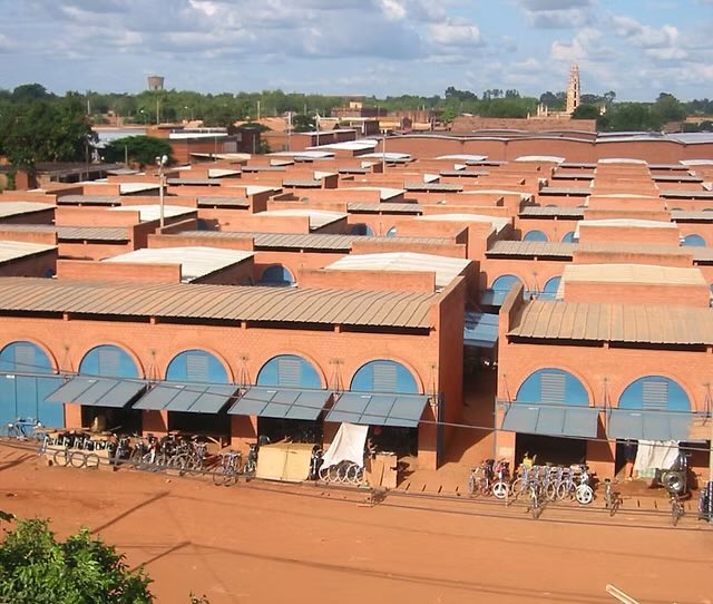 shavnyuy's tweet photo. Burkina Faso again, showing us how good infrastructure can be when you use local materials intelligently.

The Koudougou Central Market won the Aga Khan Award for Architecture. 29,000 square metres. 1,800 vendors. Primary construction material: compressed earth blocks sourced from two kilometres away. The vaulted arches were built by local enterprises with specialized earth construction expertise.

The layout does two things simultaneously; maximum commercial density and maximum natural ventilation. Two overlapping grids create shade between neighboring structures while channeling cross breezes through the alleys. The market cools itself. In Burkina Faso’s extreme heat, that’s not a design gesture, it’s survival infrastructure.

The deeper story is economic. Local materials meant local labour,  earth extraction, brick production, vault construction, all community income. A skilled workforce was trained and retained. Demand for earth construction in the region grew long after the build ended.

Then the market opened. 1,800 vendors with dignified, shaded, ventilated trading spaces. Better conditions mean longer trading hours, stable livelihoods and a neighbourhood that actually prospers. A market that works climatically is a market that works economically.

📍Koudougou Central Market, Koudougou, Burkina Faso. Laurent Séchaud / SDC.