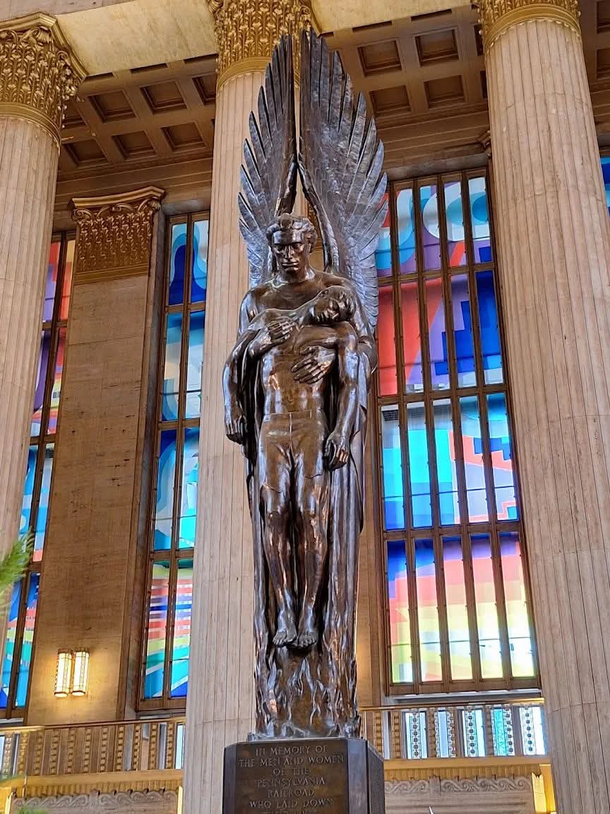 Mrstanleycup's tweet photo. This has always been my very favorite statue. Commissioned to honor the Pennsylvania Railroad employees who died in World War II, Walker Hancock’s heroic bronze presents the Archangel Michael, angel of the Resurrection, lifting a lifeless soldier in his arms. The angel’s great wings point directly upward as he frees the youth from the flames of battle. The high columns of 30th Street Station form a dramatic backdrop, and the pedestal bears the names of all 1,307 railroad employees who perished in the war. It is 39' feet tall.