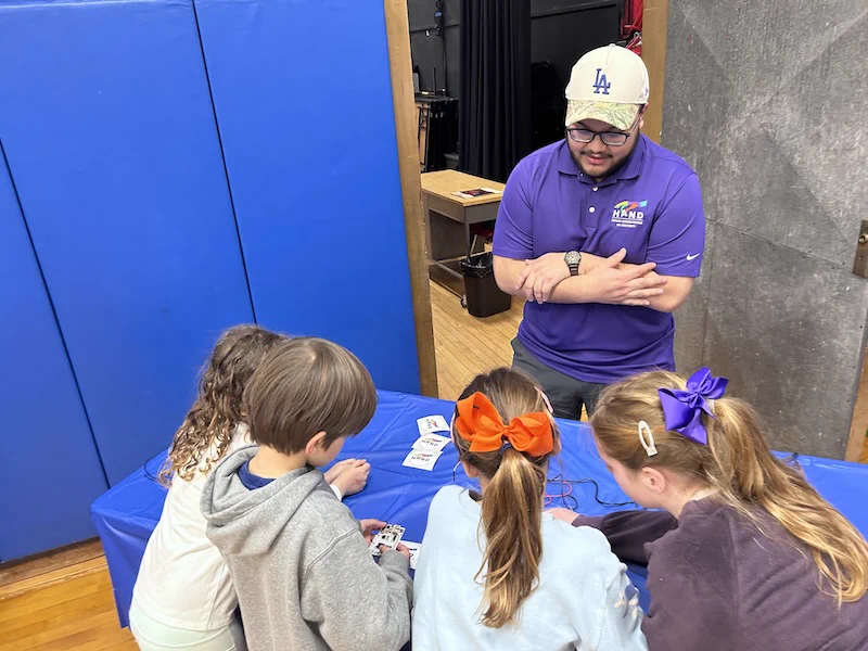 Smiling man showing a group of four students robot fingers.