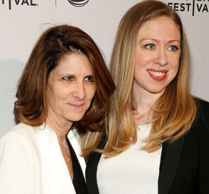 NizNellie3's tweet photo. 🚨  See this lady with Chelsea Hubbell? I mean, CLINTON, Chelsea Clinton. My apologies.

That's Linda G. Mills, the President of NYU. On her campus, a massive swastika flag was displayed over an academic building as students and their families attended a graduation event.

Her office claims they're "shocked and horrified" that someone would do such a thing. 

Last month, President Linda permitted former Columbia University professor Dr. Mohamed Abdou to speak to students on her campus. He supports terrorism.

The Egyptian-born Canadian professor not only promoted his vile hatred for America, but he went off an an anti-Semitic tirade, then spewed his affection for Hamas terrorism and their martyrs.

"Be proud of your hatred. I believe in an Islam that hates America. God damn America."

Linda's campus is on track to receive $732 MILLION in taxpayer federal funding for 2026-2027.