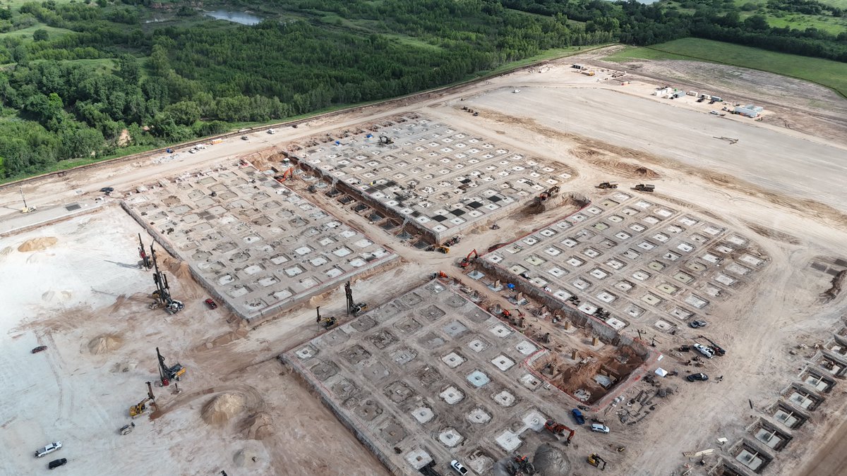 JoeTegtmeyer's tweet photo. The new Giga Texas Optimus factory foundation work continues with three distinct sections under construction. 

On the south end of what I think may be phase 1 of the construction, the large depressed graded area has had about .5 to 1 meters of gravel and crushed concrete added and now GeoPier equipment is at work. 

On the middle section, dense footings of two primary types are being constructed, suggesting heave loading of the structure in this area. 

On the north end, it’s mainly flat grade with little footing work so far. 

I say I *think* this might be a two phase construction project because the north perimeter grade beam is laid out as if it is the final configuration, but the south end is not. There is a large field south of this area that, with reclamation work, could support a doubling of the structure, if that was desired.