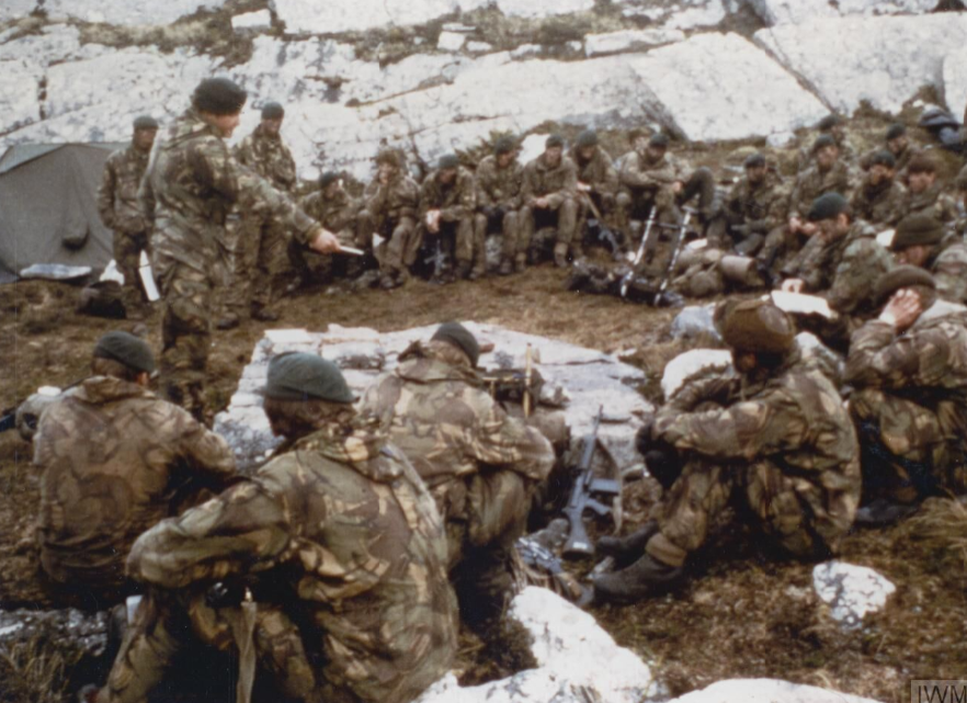 BootneckStuff's tweet photo. A bunch of Royal Marines from 3 Commando Brigade sitting in the dirt and snow on a freezing Falklands mountainside, rifles stacked, lids on, listening to their officer point at a map like it’s the most important thing in the world.

Because it was.

This is the moment before the final hammer blow. 

After days of yomping across the island in sideways rain, gale-force winds, and boots that never dried because of the honking environment these lads were now within striking distance of Port Stanley — the last Argentine stronghold and the key to ending the war.

The Argies weren't looking forward to us arriving. They knew we were coming. They didn't want to be there. 

There was no warm briefing rooms. No PowerPoint. Just an open-air huddle on the rocks, one man with a map, everyone else freezing their bollocks off but locked in for the details.  

The next 48 hours would decide everything.

They’d already fought at Goose Green, secured the outer hills, and marched further than most armies do in a month. 

Royal had been knee deep in fighting where you’re crawling through peat and rocks in the dark while the enemy hurls artillery and machine-gun fire at you.

The lads were threaders. They also wanted it to be over. 

This briefing wasn’t theory. It was “here’s the objective, here’s the route, here’s how we’re going to take it, and here’s how we’re going home.”

The Bootnecks of 42 and 45 Commando had trained for this, just without the two way range. It's what Royal does.  Cold, wet, exhausted, but completely focused. 

Probably a ton of flashing during the training, but cracking some funnies at times like we do. 

The officer pointing at the map knew every one of those men was about to risk his life on the word he was about to give.

And Royal delivered.

Two days later the Argentine garrison in Stanley surrendered. The war was over.

This photo captures a bunch of cold, muddy commandos getting their final orders before they went and finished the job.