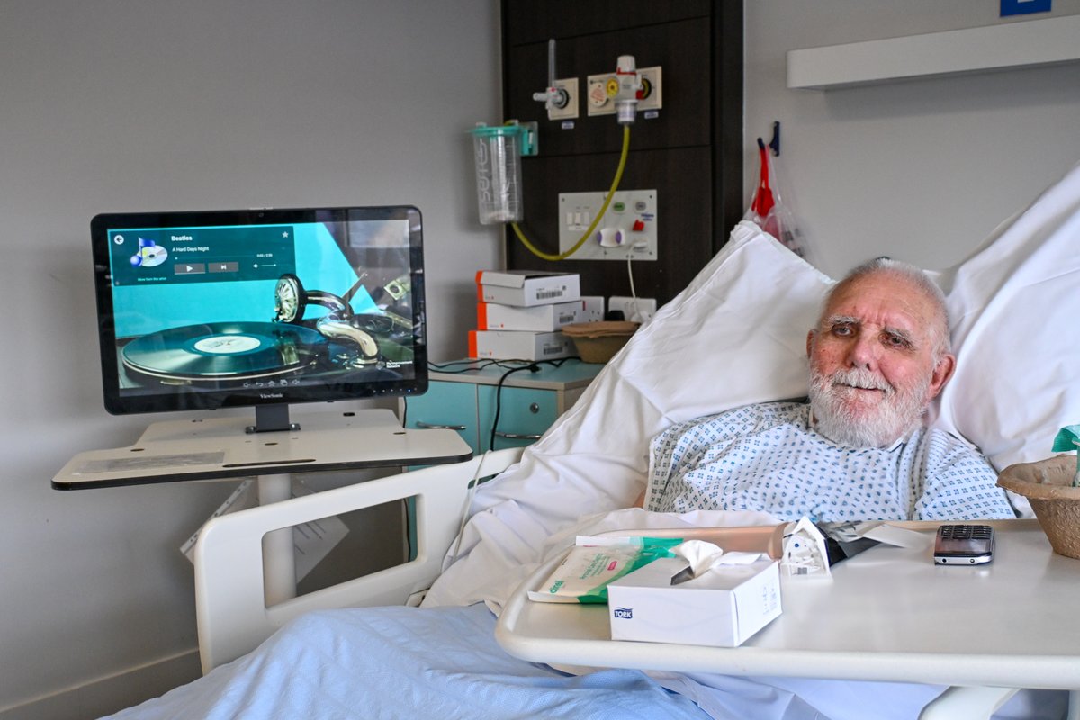 DBH_NHSFT's tweet photo. Patients with dementia, anxiety and learning disabilities are amongst those benefitting from the introduction of five therapeutic devices across Doncaster and Bassetlaw Teaching Hospitals (DBTH).

The Reminiscence Interactive Therapy Activities (RITA) device, a portable touch-screen system, offers a welcomed distraction for patients receiving enhanced care due to support their additional needs.

Previously, hospital teams closely observed patients at risk of falls and agitation, but lacked the tools to distract them, boost their mood, or help soothe anxieties, explained Julie Wragg, Corporate Nurse at DBTH.

She said: “Our teams will watch patients to prevent them falling but there isn’t always engagement with them. It can mean boring and long days for both colleagues and patients.

“RITA has opened up a way for them to pass the time and build up rapport and trust as often patients who are confused can feel vulnerable when in hospital.”

Use of the RITA also reduces the need for medication to settle those who are distressed, Julie explained.

Activities on the RITA include quizzes, interactive musical instruments and short television broadcasts from the 1950s and 60s.

88-year-old Trevor Holder, a patient on the Mallard Ward at Doncaster Royal Infirmary, particularly enjoys watching musicals on the device.

He said: “It passes the time and helps to have some entertainment while I’m here.”

Trevor has watched at least four musicals using the RITA from his bedside, including Oklahoma and Calamity Jane.

He eagerly awaits the addition of ‘Seven Brides for Seven Brothers’ to the device’s catalogue.

The RITA is not only useful for passing the time independently, but also as a group.

Sarah Gallagher, Activities Coordinator on the Mallard Ward, explained: “When I do the quizzes, I try and do it as a group and get them more involved.”

“We just did one with Trevor and another patient and now they’re chatting and have got to know one another a little bit.”

The interactive device comes with a wide range of reminiscence and therapeutic content, allowing Sarah to evoke fond memories and engage patients.

Sarah said: “The RITA helps me get into conversations with them about what they enjoy and what makes them smile.

“It gives them a little sense of being people.”

One of Sarah’s patients had emigrated to the UK. With the help of the RITA, he could see the place he had lived before and was ‘taken aback’, Sarah explained.

The RITA also aids communication for patients who have difficulties speaking or describing things.

Sarah said: “Patients can use a special photo of a body on the RITA to point to or show where they may be hurting.”

The introduction of the RITA devices was only possible thanks to the generosity of the local community and Doncaster and Bassetlaw Teaching Hospitals (DBTH) Charity.

Julie said: “Knowing that the community has funded this is hugely heart-warming and they themselves may just benefit from RITA in any potential future admissions.”

Visit the charity website to find out more: https://t.co/MgHezudyyW