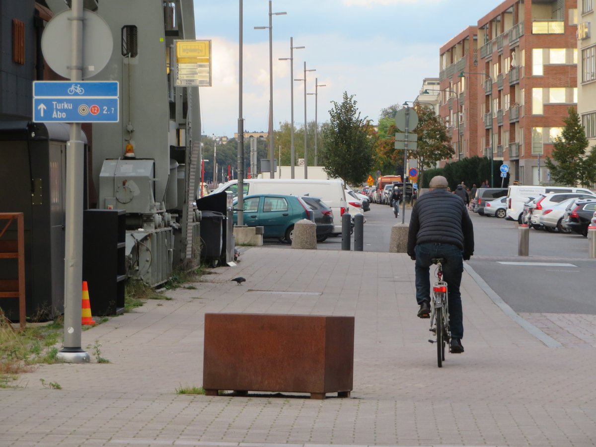 TJTurkula's tweet photo. Iltakävelyiltä havaintoja reitillä Kaarle Knuutinpojan rantatie - Telakkaranta - Vanha Hirvensalontie - Kölikatu - Kaarle Knuutinpojan rantatie.  Osa 3(7): Väärin sijoitettu pyöräilyn suunnistuskyltti "houkuttelee" pyöräilijöitä ja skuuttaajia ajamaan jalkakäytävällä ja pysäkillä.

Kyseisen liikennemerkin kohdalla pyörätie päättyy ja jalkakäytävä alkaa. Mistä satunnainen pyöräilijä tietää asian. Fiksu oivaltaa, että pysäkin täytyy olla jalkakäytävä, mutta suuri osa porhaltaa pyörällä tai skuutilla kovaa vauhtia pysäkille.
Turun kaupungin palautesivuilla olen kahdesti pyytänyt siirtämään pyöräilyn suunnistuskyltin kadun vasemmasta reunasta oikeaan reunaan, mihin se tieliikennelainkin mukaan kuuluisi.

Vasemmalla olevan pylvääseen pitäisi laittaa jalkakäytävä-liikennemerkki, koska pyörätie päättyy kyseisessä kohdassa, jossa alkaa jalkakäytävä ja bussipysäkki. Kaupungilta ei mitään parannusta tilanteeseen. Kaupunki huomautti: "Jalankulkijan pitää kuulemma ottaa huomioon muut kulkijat." Pitääkö jalkakäytävällä kävelevän ottaa huomioon myös ajoneuvot, kuten pyörät ja skuutit, joilla ajaminen on jalkakäytävällä ja pysäkillä kielletty?  Vastattu: 30.6.2025: "Kiitos palautteestanne! Turvallinen ja sujuva liikkuminen edellyttää huomaavaisuutta ja varovaisuutta kaikilta kadunkäyttäjiltä. Valitettavasti joukkoon mahtuu aina niitä, jotka eivät piittaa liikennesäännöistä ja ajavat kohtuuttoman kovaa huomioimatta muita. Liikennemerkkejä ja erilaisia tiemerkintöjä lisäämällä ja siirtämällä ei valitettavasti saada poistettua häiriökäyttäytymistä." Ystävällisin terveisin Liikennesuunnittelu 

Oheinen vastaus on yhtä tyhjän kanssa! Outo vastaus. Ajoneuvoliikenne, kuten pyöräily ja skuuttailu on jalkakäytävällä ja pysäkillä jyrkästi kielletty. Pitääkö jalankulkijan varoa ajoneuvoja jalkakäytävällä ja pysäkillä? 

Odottaako Turun kaupunki hautakivimääräystä?  Läheltä piti. Kävelin kerran Ravintola Nobin pohjoispuolelta joen suuhun päin. Olin lähellä Nobin pohjoista terassikoppia Nobin pohjoisen sisäänkäynnin vieressä. Kopin takaa porhalsi sähköpyöräilijä kovaa vauhtia vastaan jalkakäytävän ja pysäkin vasenta reunaa.
Olin vähällä jäädä sähköpyöräilijän alle. Jos olisin ollut puolisen metriä edempänä, sähköpyöräilijä olisi törmännyt minuun kovalla vauhdilla. Pyörä taisi olla viritetty, kun vauhti oli niin hirmuinen. Jos kolari olisi tapahtunut, olisin varmaan loukkaantunut vakavasti tai kuollut. Jalankulkija ei osaa varautua tällaiseen hurjasteluun jalkakäytävällä kopin takaa huonon näkyvyyden vallitessa.

Jokisuuhun päin jalkakäytävä-liikennemerkki on saatava myös ravintola Nobin pohjoispuolen rantaväylälle Purserinpolusta alkaen ja uudelleen Ravintola Nobin pohjoispäähän.

Tänään kävellessä olin jäädä polkupyörän alle Nobin pysäkin kohdalla, kun pyöräilijät kaahasivat kovaa vauhtia jalkakäytävällä kovaa vauhtia jokisuuhun päin. Kyseisellä paikalla ajoradan ja jalkakäytävän väliset kanttikivet ovat matalat, joten suuri osa pyöräiljöistä ei ymmärrä, että pysäkki on jalkakäytävä. Väylän merkintöjä tulisi pikaisesti parantaa ennen kuin rysähtää.

Miten Turun kaupunki voi järjestää tällaisia miinoja jalankulkijoille eikä suostu tekemään mitään parannusta liikenneturvallisuuden parantamisesksi. Argh!