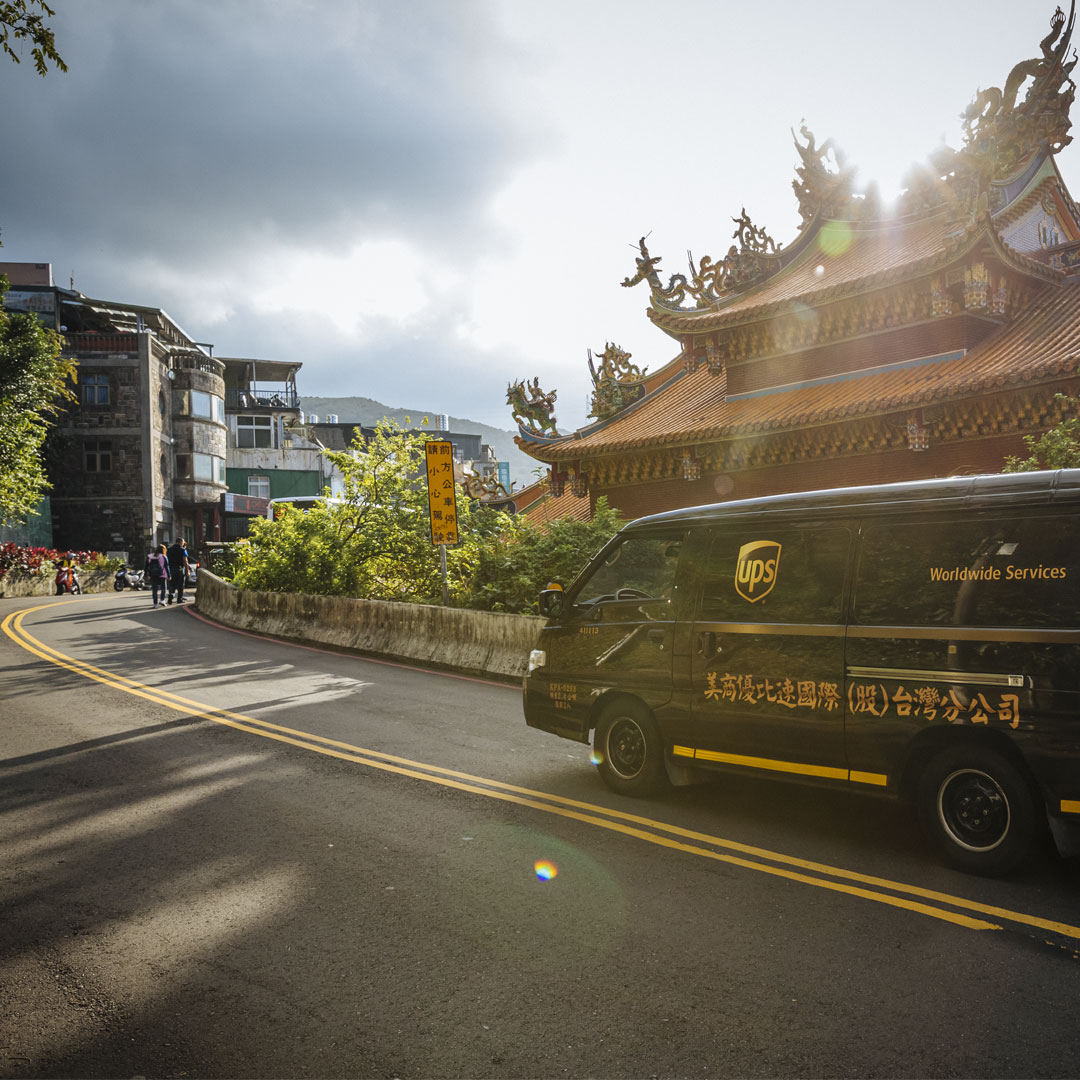 UPS van driving in Taipei near a traditional East Asian temple on a curving road.