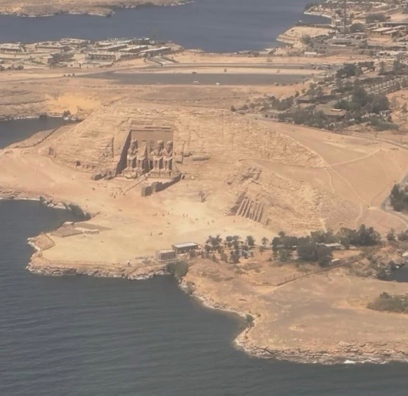 historyinmemes's tweet photo. Aerial view of Abu Simbel Temple from an airplane over Aswan, Egypt.

Approaching Abu Simbel Airport offers an extraordinary aerial perspective of Egypt’s iconic rock-cut temples, perched along the shores of Lake Nasser. From a plane window, the endless desert suddenly gives way to the lake’s deep blue waters, where the monumental temples of Ramesses II and Nefertari appear carved directly into the golden sandstone landscape.

This rare viewpoint emphasizes the immense scale of the ancient complex and reveals the man-made hill created behind it during UNESCO’s ambitious relocation project in the 1960s. Travelers flying from Aswan can often enjoy the best views by choosing a window seat on the left side of the aircraft, as planes frequently pass over the lake and the temples during their approach to landing.