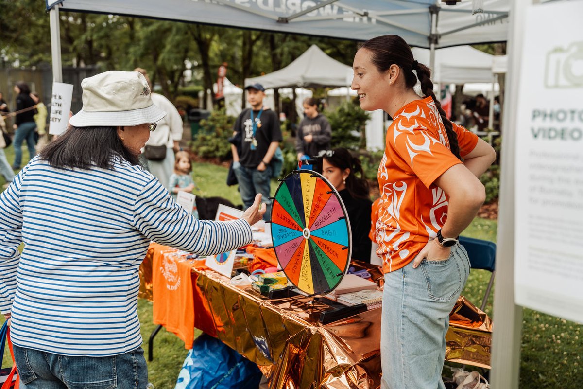 Person spinning a colorful wheel at an outdoor event booth during National Indigenous Peoples Day.