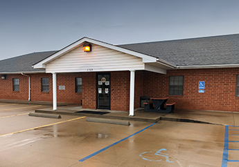 Single-story brick building with a covered entrance and accessible parking spaces on a wet concrete lot.