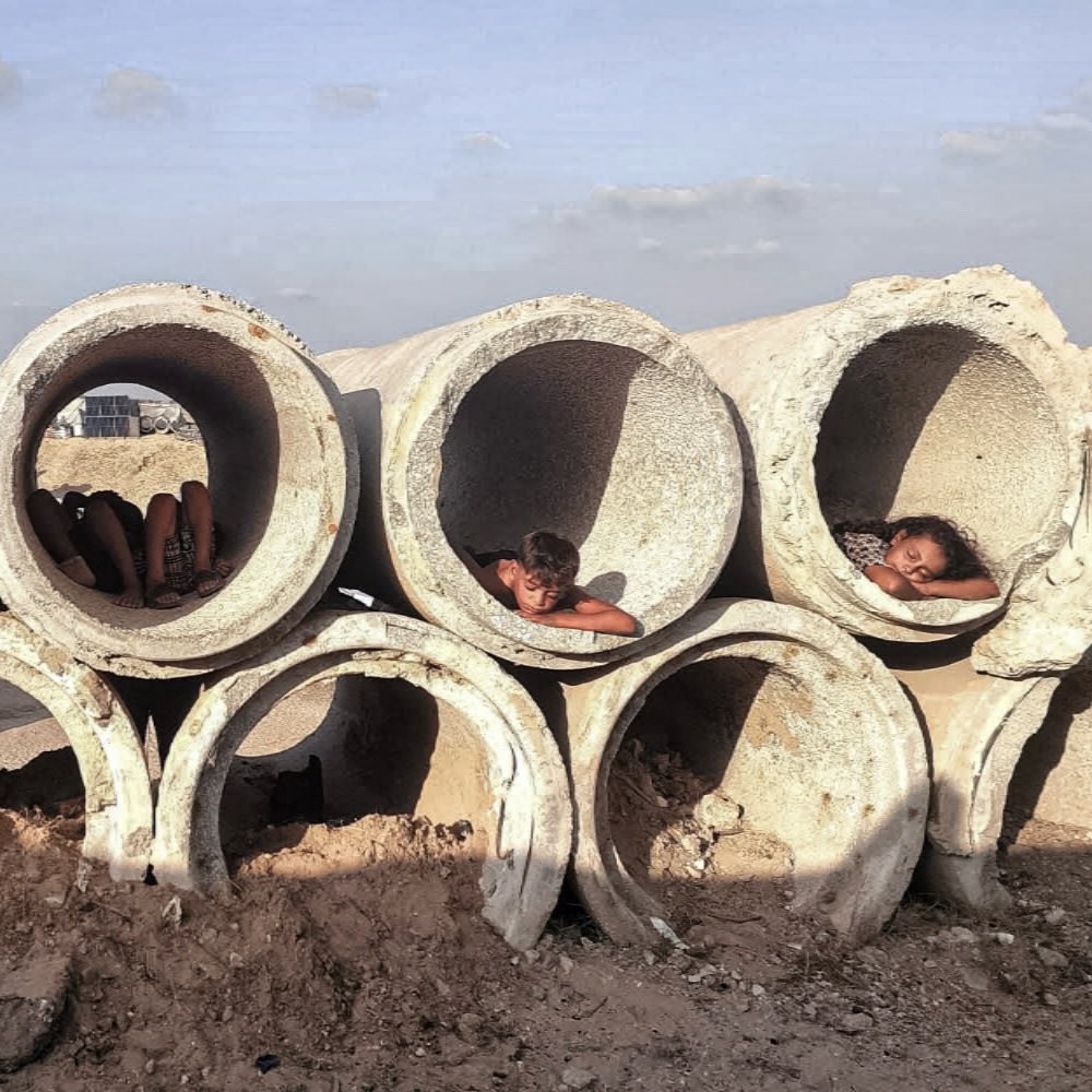 Timesofgaza's tweet photo. Children and young people in Gaza flee the heat of the tents to unused concrete pipes, finding temporary shade there instead of shelter. https://t.co/XscjBuHO5c