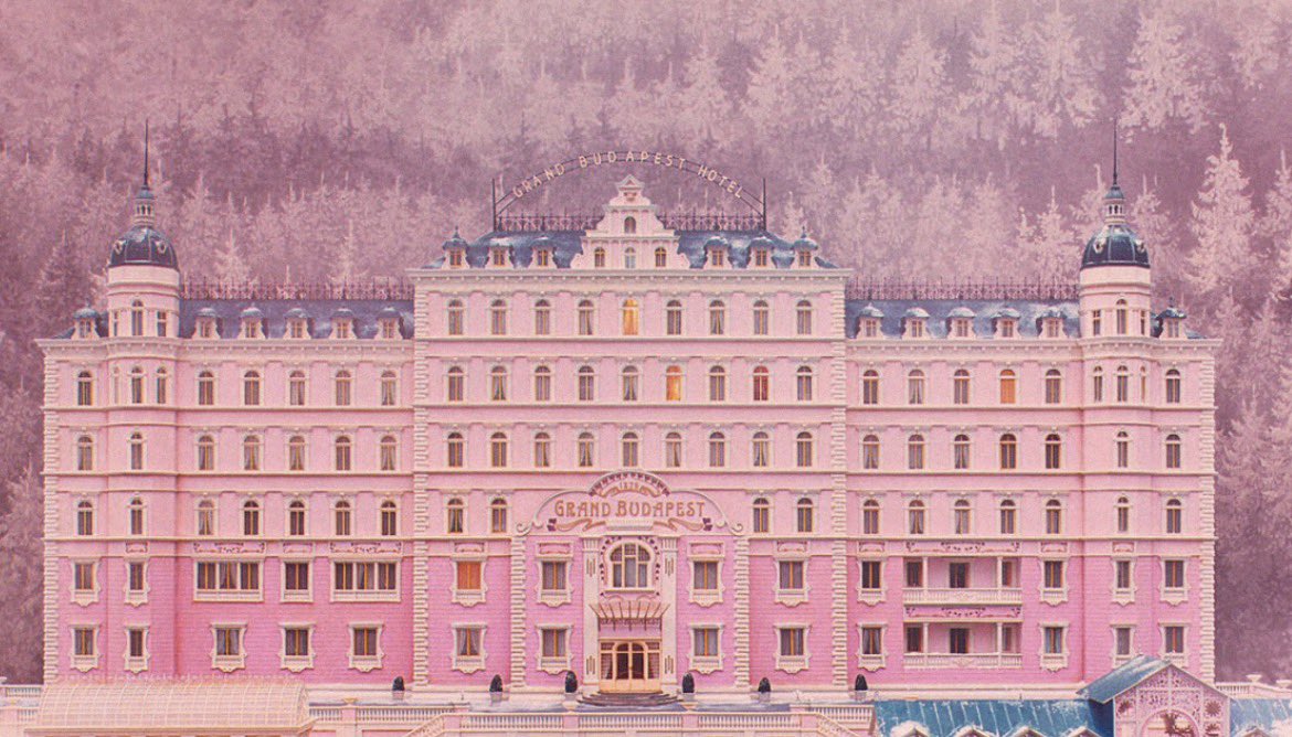 valentinakulaga's tweet photo. One of my favorite shots in all of cinema: the Grand Budapest Hotel, by Wes Anderson, one of the directors I admire most.

Everything about the frame is deliberate. The hotel sits dead center, perfectly symmetrical, every window and balcony mirrored on either side. The palette is unmistakably his: soft rose pinks against the muted lavender of a snowy forest, the whole image bathed in a faded, almost nostalgic light. It feels less like a photograph and more like a memory.

What few people realize is that the hotel was never real. It exists only as a handcrafted miniature, a scale model filmed to feel monumental. No grand building somewhere in Europe, no towering set. Anderson deliberately chose to build it by hand rather than render it digitally, and that decision is precisely why it feels so alive. There is a warmth to it that no computer has quite learned to imitate.

And that, to me, is the quiet genius of it. The idea of “a film about a hotel” is ordinary; anyone could propose it. But this particular world, its color, its symmetry, its melancholy, is something else entirely. That is vision: the ability to take a modest idea and shepherd it into something people fall in love with.

A small pink model that does not exist in any real place now lives permanently in the memory of millions. That is the whole magic of it.