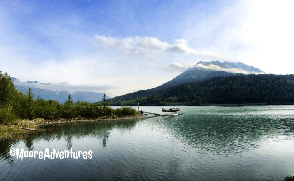 MooreAdventurAK's tweet photo. Red floatplane on flat water with mountains going straight up behind it into the clouds. You don't go looking for views like this — they show up right off the road and you just pull over. https://t.co/tO6V5VF1xI