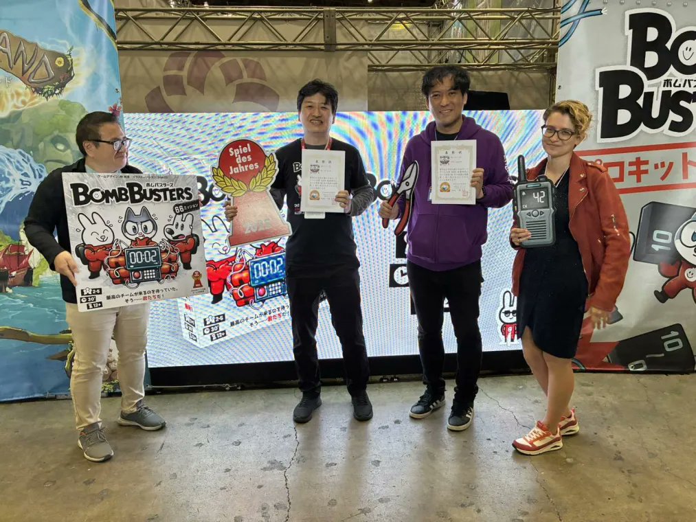 EngamesToyama's tweet photo. 「世界のボードゲームを広める会 ゆうもあ」様が主催する「日本ボードゲーム大賞2025」の投票部門でボムバスターズが最多得票数となる大賞を授賞しました。
授賞を記念して、主催者様よりゲームマーケット会場にて代表・杉木とゲームデザインを担当された林尚志さん（OKAZU brand）に賞状をいただきました。
販売元であるCocktail GamesのJulia KLOKOVAさんにも同席していただきました。