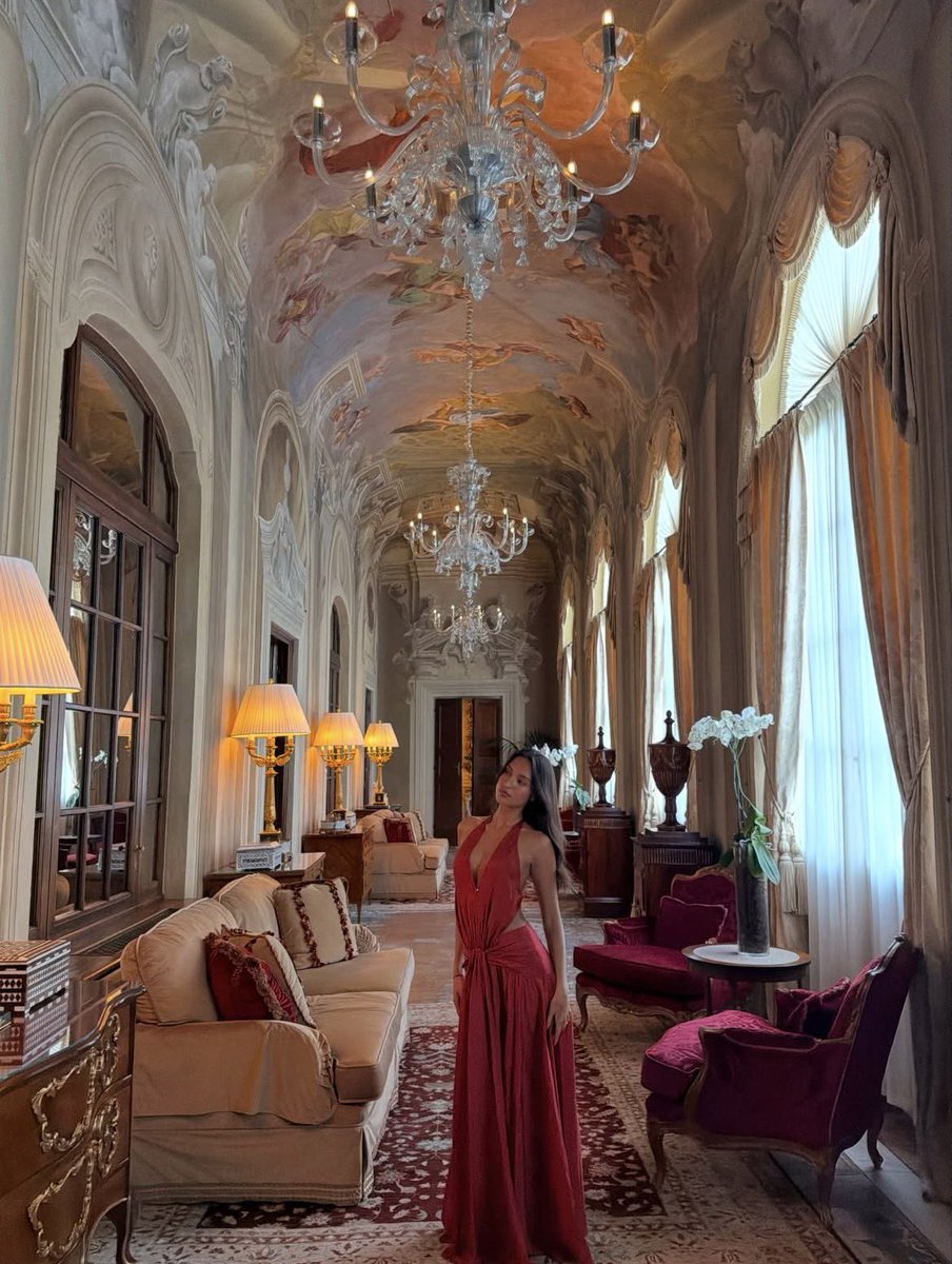 arexandra's tweet photo. I feel like I’ve stepped into another era of pure elegance. The way the light dances off the chandeliers and frescoed ceilings makes my heart flutter. Wearing this flowing red dress, I’m completely lost in the timeless beauty surrounding me. https://t.co/F2RUyIDLFg