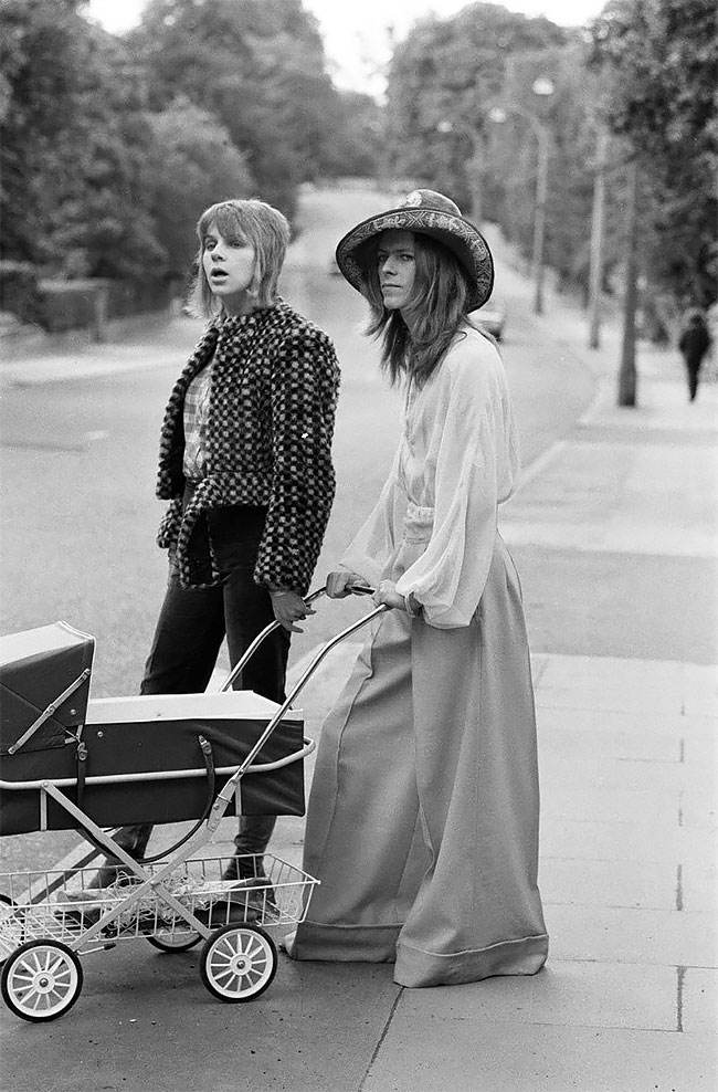 ankorinclan's tweet photo. En la primavera de 1962, dos chicos de 15 años se pelearon por una chica en Bromley, al sur de Londres. Uno de ellos era David Jones, que pronto cambiaría su apellido a Bowie. El otro era su amigo George Underwood. Un golpe accidental de la uña de Underwood le arañó la córnea y paralizó los músculos del iris del ojo izquierdo. Cuatro meses de hospital. Pupila izquierda permanentemente dilatada para el resto de su vida.

Bowie, años después, le dijo a Underwood que le agradecía el golpe. Que le había dado "una especie de mística."

El mundo creyó durante décadas que Bowie tenía los ojos de dos colores distintos. No era heterocromía. Era anisocoria: una pupila fija, incapaz de responder a la luz, que hacía que un ojo pareciera oscuro y el otro azul dependiendo del ángulo y el flash. Sus dos ojos eran azules. Solo uno respondía al mundo. El accidente con su amigo le dejó en el rostro exactamente el tipo de anomalía visual que encajaría perfectamente con cada personaje que construiría después.

Como si hasta su cara hubiera decidido participar en el proyecto.

La fotografía de 1971 lo muestra en la calle, con Angie Bowie a su lado y el cochecito donde viaja Zowie, el niño que décadas después se convertiría en el director de cine Duncan Jones, conocido por Moon y Source Code. Bowie lleva una prenda estampada, sombrero, y la misma expresión de quien no ha considerado en ningún momento que su aspecto necesite justificación.

En ese año Bowie tenía 24 años y estaba construyendo algo que no tenía nombre todavía. Hunky Dory saldría en diciembre de ese año. Ziggy Stardust llegaría en 1972. La moda, el teatro, el maquillaje y la ambigüedad sexual eran para él herramientas de composición, no provocaciones calculadas para escandalizar. "No me importaba lo que pensara la gente", le dijo a la revista Rolling Stone en 1976. "Nunca lo hizo."

Lo que hizo durante los 70 no fue ponerse disfraces. Fue demostrar que la identidad podía ser una práctica artística continua, no una condena fija.

La foto de 1971 tiene algo de manifiesto silencioso. No hay escenario, no hay luces, no hay público esperando. Solo una calle, una familia joven y un hombre que empuja un cochecito con la misma presencia con la que más tarde llenaría estadios.

Bowie no hacía que la rareza pareciera un disfraz.

La hacía parecer lo más normal del mundo.