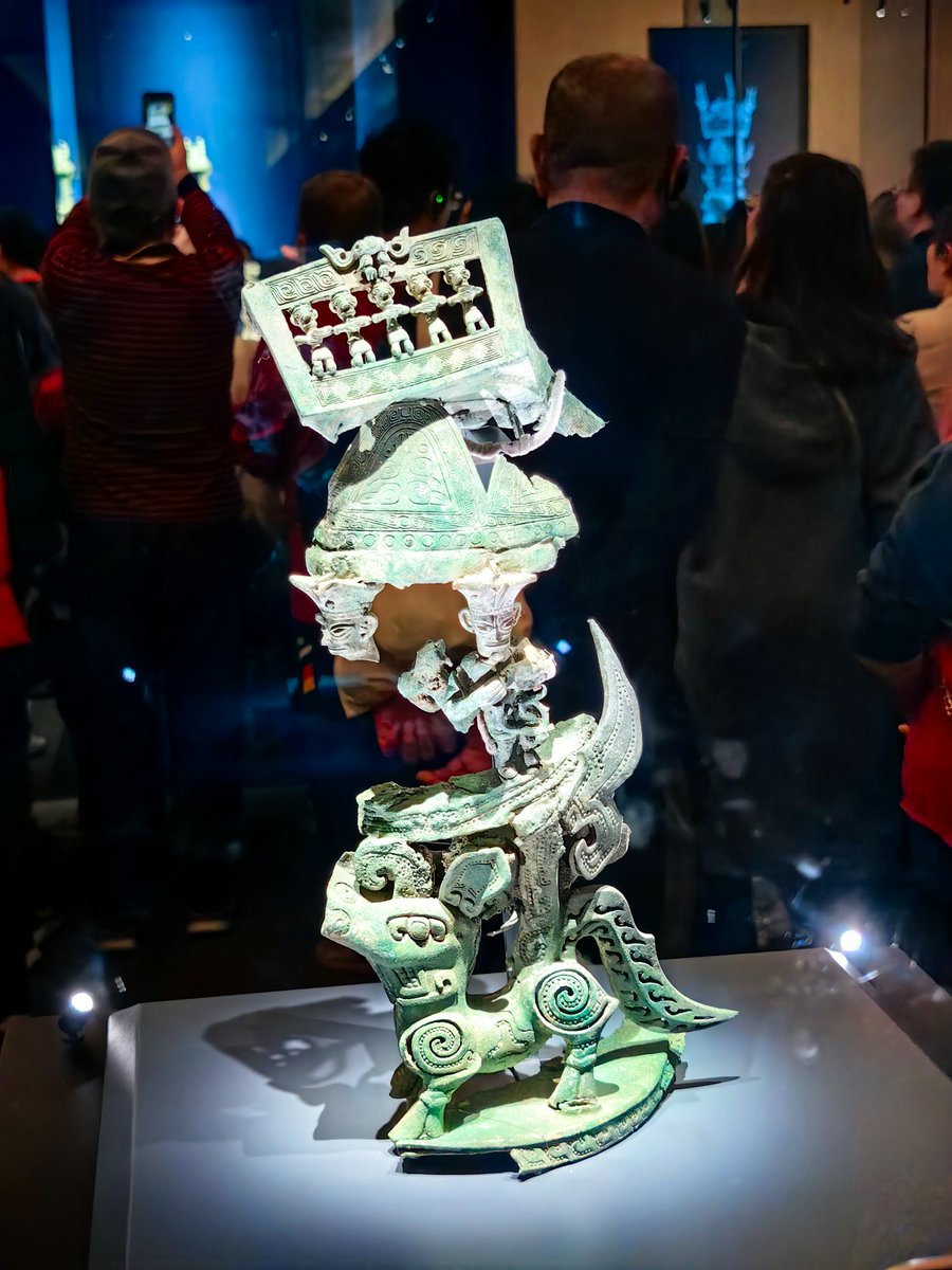 ZhaiXiang5's tweet photo. More than 3,000 years ago, the people of Sanxingdui may have created a "flying altar."

It had a divine dog crying out with wings spread, solemn figures making offerings, mysterious images of sacred mountains, and a strange creature with a human face and a bird's body looking down at the human world.

In 1986, this bronze fragment was unearthed from Pit No. 2 at Sanxingdui and named the "Altar." Although one half had been melted away, smashed, or placed elsewhere, and the remaining half had also been warped by fire, what survives still allows us to see traces of the extraordinarily astonishing imagination of the ancient Sanxingdui people.

At the very bottom of this altar is a bronze dog.

Its mouth is rectangular, a feature shared by all the bronze dogs discovered at Sanxingdui so far. A credible interpretation is that this shape may depict the dog crying out loudly, so that its voice could reach the gods.

On the dog's forehead is a horn resembling an elephant's trunk. But even this is not the most striking feature of the creature. On its back is a wing raised upward, suggesting that it could not only send its voice up to the deities above, but also spread its wings and fly toward their dwelling place.

Above the dog stand human figures. They wear short-sleeved garments with hems reaching their knees, and their hands are held before their chests, grasping what appear to be vine-like objects.

Even more mysteriously, two of these figures have human faces appearing on their hats. Together they carry four mountain-shaped objects, each decorated with a beast motif.

Above the four sacred mountains is a roof. On each side of the roof is a row of kneeling figures, while at the very top stands a strange creature with a human face and a bird's body. Each of the four sides also features a bird, decorated with dragon patterns.

The surviving height of this artifact is 55.3 centimeters.

Today, we can only see its fire-damaged remains. The six newly excavated sacrificial pits from five years ago allowed many once-fragmented artifacts to be reassembled. Yet this piece still awaits its missing parts.

Even so, the part that remains is enough to astonish us 3,000 years later.

We find Avatar breathtaking because it created a fantastical universe in which humans are connected with nature, ancestors, and spirits.

But more than 3,000 years ago, Sanxingdui had already used bronze, divine dogs, flying wings, sacred mountains, and bird-gods to construct their own "Pandora."

What we see is only a damaged bronze artifact.

What they saw may have been an entire universe.