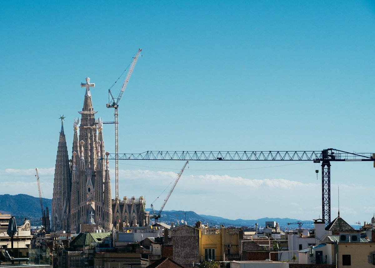 Nuts_thePhantom's tweet photo. Barcelona 025

カサ・ミラの居住スペースを抜け、さらに上へと階段を上がる。
そこに広がっていたのは、270ものレンガ造りのアーチが連なる、通称「クジラの胎内」と呼ばれる屋根裏空間。ガウディが紐と重り（チェーン）を逆さに吊るして、最も自然で美しい建物の重力バランスを導き出した「フニクラ模型」も展示されていて、彼の狂気的なまでの天才ぶりに息を呑む。

そして、いよいよ光が降り注ぐ屋上へ。
青空に向かってニョキニョキとそびえ立つのは、まるで兜をかぶった騎士のような不思議な造形の煙突たち。
屋上の波打つ床を歩いていると、アーチの隙間や、まるで覗き穴のようになっている不思議な開口部があることに気づく。

気になってそこからそっと向こう側を覗いてみて、思わずハッとした。
切り取られた額縁のような視線の先にまっすぐ見えたのは、遠くにそびえ立つサグラダ・ファミリア。
ただの気まぐれなデザインではなく、「ここから覗いたときに何が見えるか」という景色まで、すべてガウディの設計の一部だったんだと確信した瞬間、全身に鳥肌が立った。

100年以上も前に、こんなロマンチックで完璧な仕掛けを街の中に仕込んだガウディ。
バルセロナの心地いい風に吹かれながら、その天才の思考の深さにすっかり脱帽してしまった。