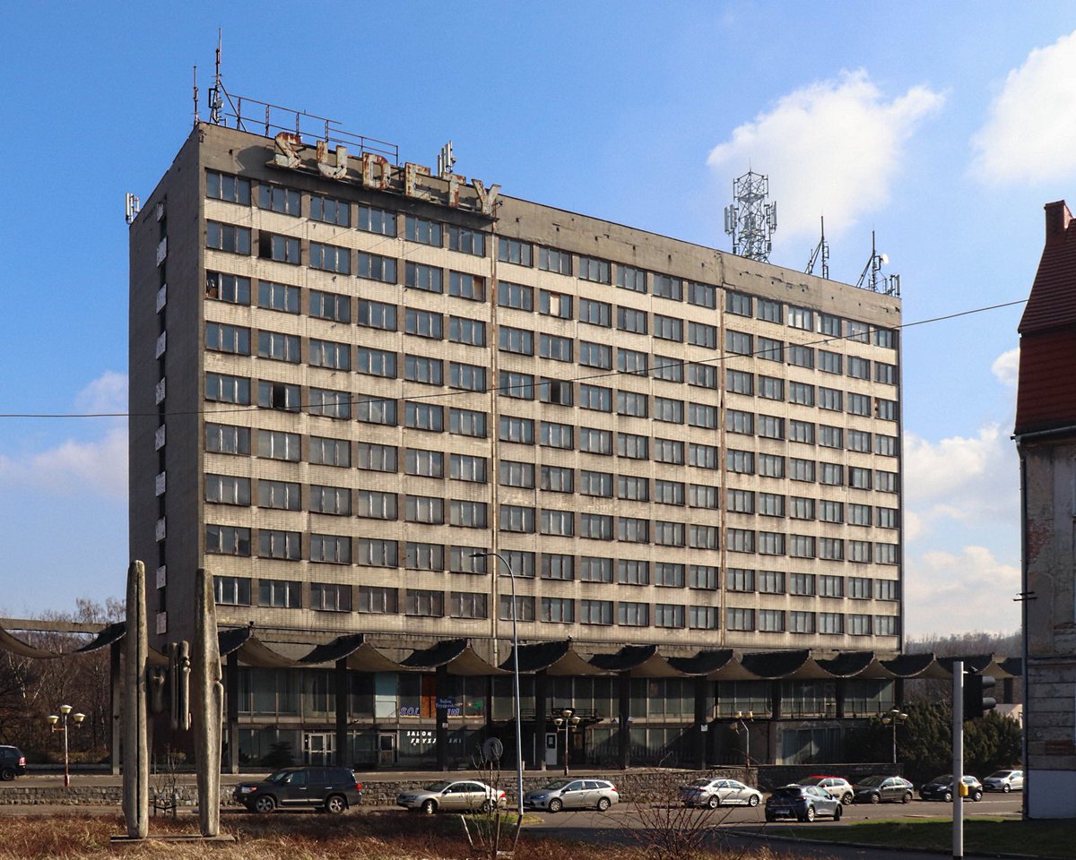 olasempruch's tweet photo. Hotel Sudety. Czasy górniczej prosperity, pod koniec lat 60. Wałbrzych się rozrasta,  powstają nowe osiedla i budzi się pomysł budowy hotelu, który ma być wizytówką całego regionu.

Stary hotel Grunwald przy placu Grunwaldzkim, choć elegancki, był już za ciasny i za stary na nowe czasy. Na terenie Starego Zdroju, przy ulicy Parkowej, według projektu architekta Zdzisława Pawlaka stanął więc jedenastopiętrowy kolos  - największy i najnowocześniejszy hotel w całym województwie.

278 pokoi, każdy z łazienką, telefonem i radiem. Apartamenty z telewizorem. Na dole restauracja na 300 osób, fryzjer, Pewex, wymiana walut. Za budynkiem fontanna, ogród, alejki. Prawdziwy luksus jak na tamte czasy.

Otwarcie w marcu 1971 było wielkim wydarzeniem. Przez kolejne lata przewijały się tu największe gwiazdy: Niemen, Sipińska, Zaucha, Wodecki, Lady Pank. Pracowali tu wybitni kucharze i kelnerzy jak Stefan Lawer, który podobno zainspirował samego Henryka Worcella od “Zaklętych rewirów”.

Hotel żył jednak też swoim drugim, mroczniejszym życiem: cinkciarze, politycy, spotkania w sprawie ustawianych meczy. Mówi się, że to właśnie stąd wziął się pomysł na scenariusz Piłkarskiego Pokera.

Potem upadek kopalni. Hotel stał się ciężarem nie do udźwignięcia. W 2004 zamknięto go z powodu niespełnienia norm przeciwpożarowych.

Dziś stoi pusty. Nowy właściciel z Sosnowca zarabia jedynie na antenach telekomunikacyjnych na dachu. Fontanna znikła, ogród zarósł, neony gasną.