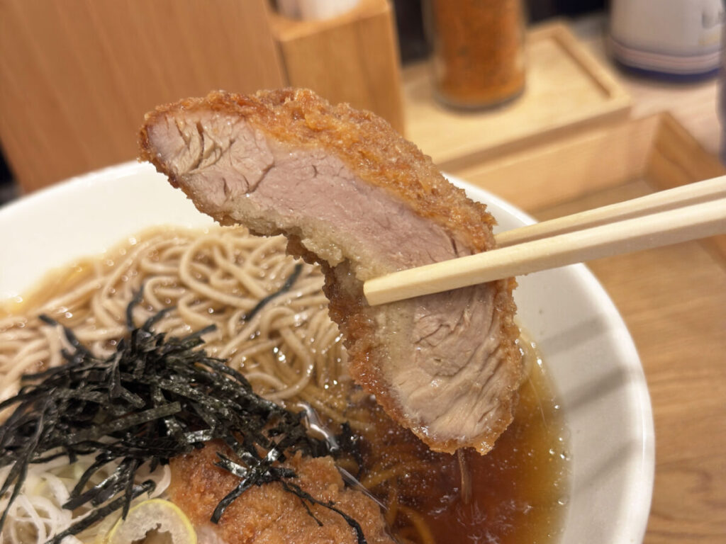akabanemagazine's tweet photo. 赤羽ララガーデン「中村麺兵衛」で食べた『とんかつ出汁そば』。

お蕎麦にとんかつ！？というなかなか攻めた組み合わせにワクワクしながら待っていると、運ばれてきたのは存在感たっぷりの一杯。

お箸で持ち上げると、ずしっと伝わる重量感！そのままお出汁にたっぷり浸して、衣にじゅわっと吸わせてからがぶり。

おっ、お肉柔らか〜！これはいいぞ！

とんかつと蕎麦って別々で食べるイメージが強かったけど、出汁をまとったカツが妙にしっくりくるんです。

また、天かすではなく、とんかつの衣がお出汁と絡む感じがなんとも新鮮。