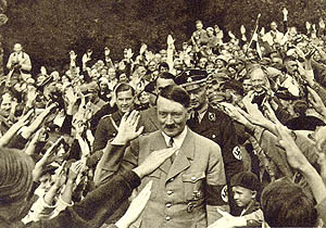 AdamMossoff's tweet photo. @Pro__Trading People standing up with arms raised in celebratory adulation when a man with likes a Totenkopf and who peddles conspiracy theories about Jews and wealthy financiers controlling politics walks into a room. It reminds me of something.... https://t.co/cyjw5FV6mv