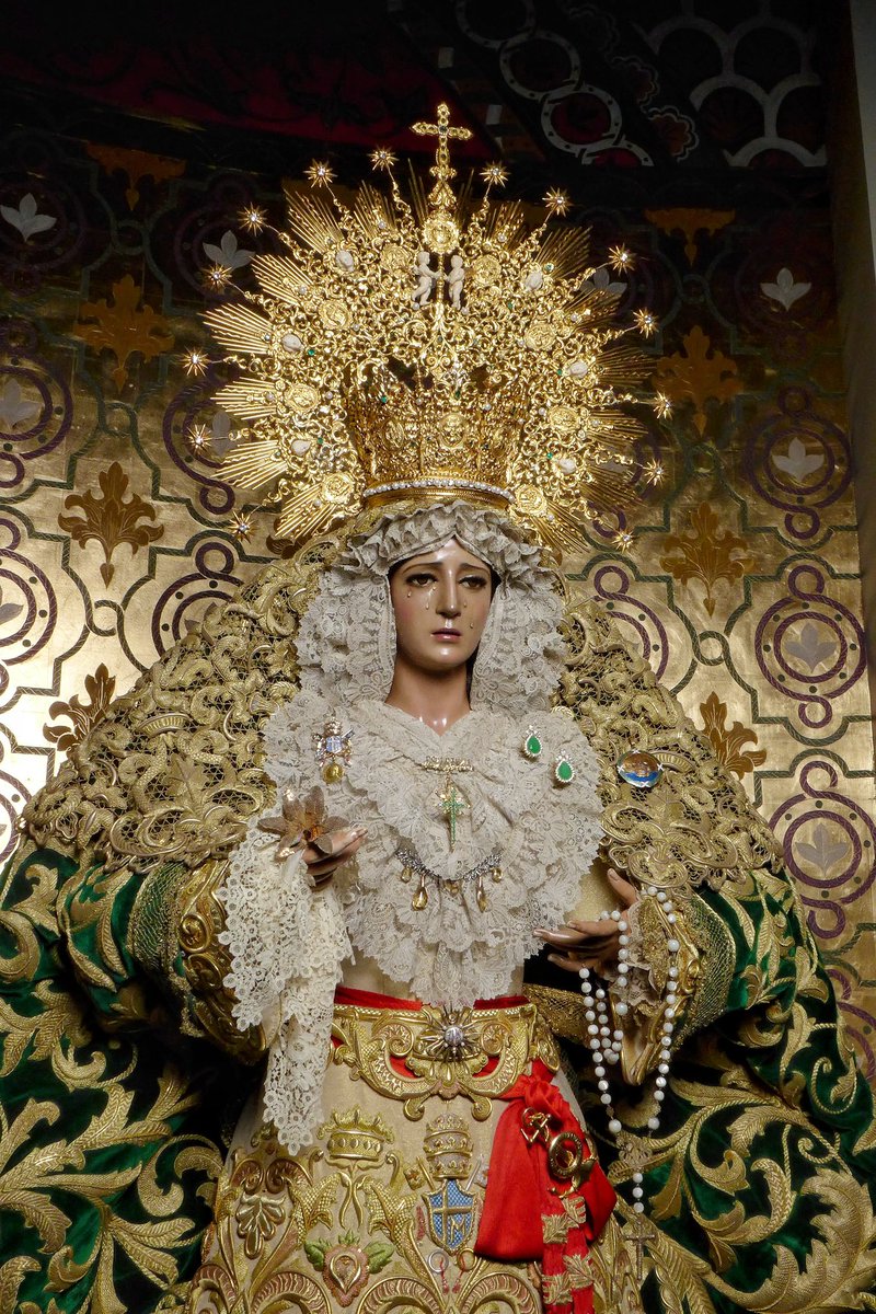pasoyesperanza's tweet photo. 𝐌𝐚𝐫𝐢́𝐚 𝐒𝐚𝐧𝐭𝐢́𝐬𝐢𝐦𝐚 𝐝𝐞 𝐥𝐚 𝐄𝐬𝐩𝐞𝐫𝐚𝐧𝐳𝐚, 𝟑𝟖 𝐚𝐧̃𝐨𝐬 𝐜𝐨𝐫𝐨𝐧𝐚𝐝𝐚.

Nuestra Titular se presenta ante sus fieles con el vestido que se le ofreció para el XXV Aniversario de la Coronación, regalo de devotos, bordado por el taller de Manuel Mendoza. 

El rostro de la Virgen se ve enmarcado por un encaje de Bruselas de punto de aguja, confeccionado en el siglo XVIII y el más antiguo que posee la Virgen. La toca, regalo de un devoto de la Virgen, fue bordada por el taller de Manuel Mendoza. Porta sobre sus sienes corona en plata de ley sobredorada, ejecutada por Orfebrería Villarreal según diseño de Juan Casielles del Nido (1963).

En su mano diestra porta un pañuelo de encaje honiton, un encaje inglés antiguo que puso de moda la Reina Victoria de Inglaterra en su vestido de novia, regalo de unos hermanos de la Cofradía; así como una azucena de oro, regalo por su Coronación Canónica y que fue realizada por las hermanas Martín Cruz.

Su talle es ceñido por el fajín de S. M. El Rey de España, manifestación del estrecho vínculo con la Casa Real.

Nuestra Amantísima Titular lleva consigo la medalla de oro de la ciudad de Málaga, símbolo de devoción del pueblo que recibió en su Coronación Canónica.

📸 @FernandoRUIzNar 
#CofradíasMLG