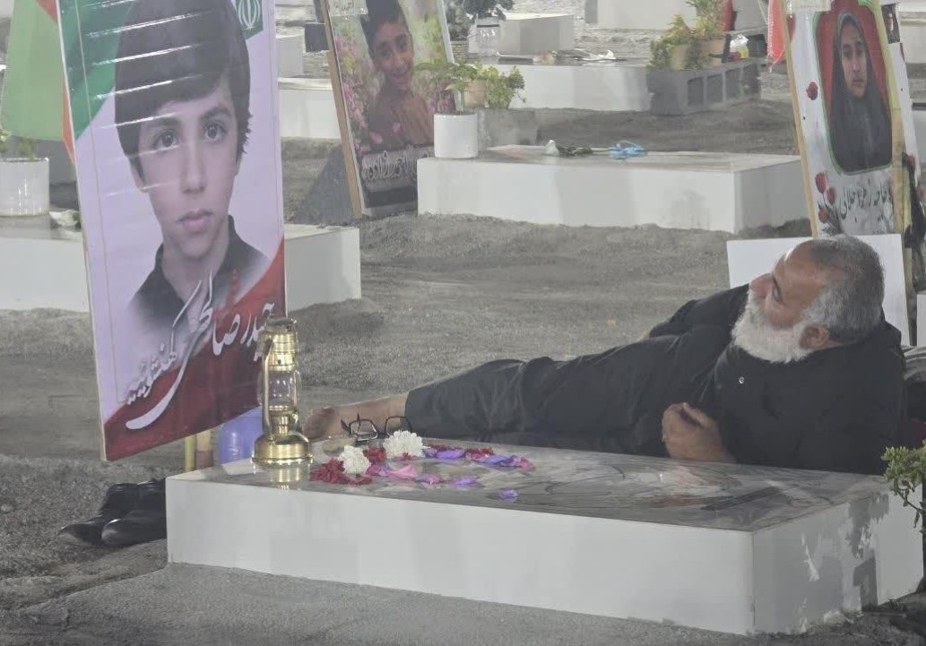 SprinterPress's tweet photo. 🇮🇷 A photo that makes everyone's eyes well up with tears when they look at it. 

A father who sleeps next to the grave of his son, who was killed by the US and Israeli regimes in a school in the city of Minab, every night. https://t.co/JBvnaaC40g