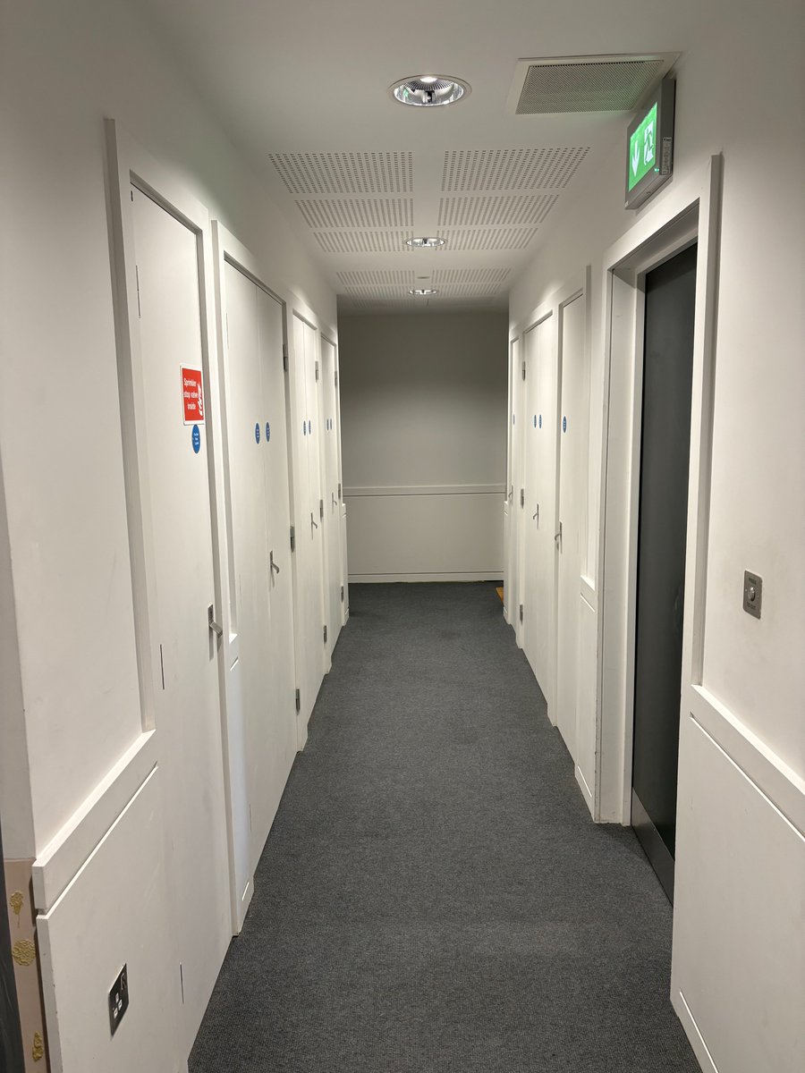 culturaltutor's tweet photo. The second photo is from a "stunning" and "beautifully presented" new apartment building in London.

Backrooms (and similar films/shows like Severance) prove that the way we design most interiors is genuinely frightening and bad for our psychological health.

Grey carpets, grey chairs, plain walls, plain furniture, square ceiling tiles, and bright lights are not good for our humanity.

But what's strange is that these bland environments (and similar bland commercial/public spaces) are actually "better" from a certain point of view.

Everything here is supposedly "cheaper" than the alternatives and also better for maintenance (i.e. less work to maintain). 

In other words, bland design is more "cost-effective", and because being "cost-effective" is what we value most... this is what we end up building everywhere, even though nobody particularly wants it.

If these places had warmer colours, maybe even some pattern, cornices, mouldings round the doors etc. then they would be more expensive, but they'd also be less damaging to our psychological health.

What makes people less stressed and less anxious is obviously better in the long-run, but it's harder to put on a spreadsheet and therefore it isn't usually factored in.

And so "more expensive" or "harder to maintain" aren't absolutes so much as expressions of priority; the initial cost of material is lower (e.g. standard pure white paint or standard LEDs) but the long-term cost to human joy, peace of mind, and happiness is way higher.

To put all of that another way: the only reason an aesthetic is disconcerting/frightening in films is because they're disconcerting/frightening in real life, and yet we keep using those aesthetics to design the world we're all actually living in!